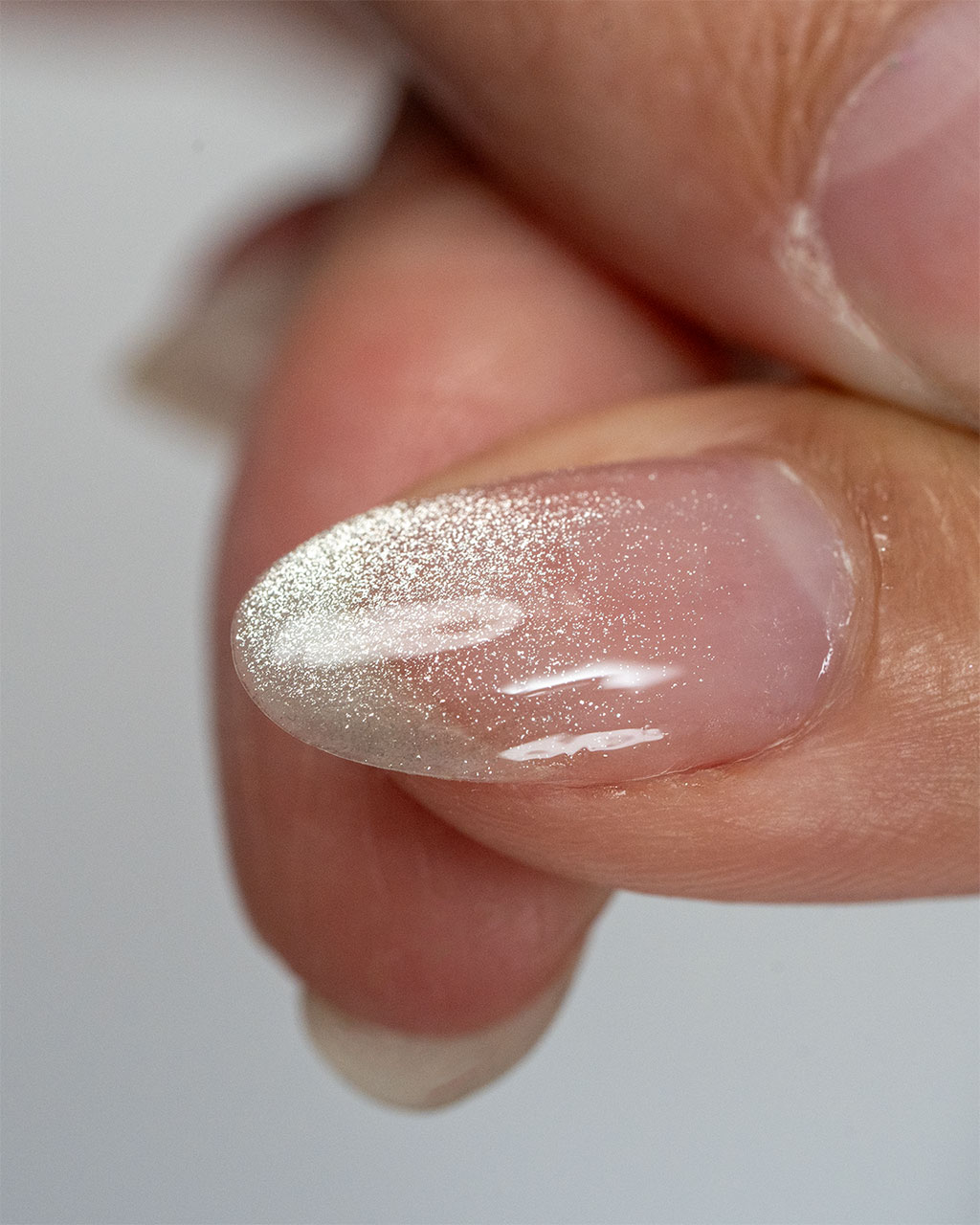 A macro photograph of a natural-looking almond-shaped nail with a delicate silver glitter ombre effect at the tip.