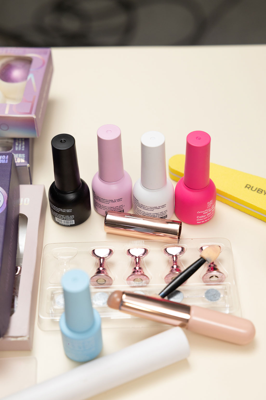A collection of nail art supplies laid out on a table, including several bottles of colorful gel polish, an ombre brush, nail stands, and a file.
