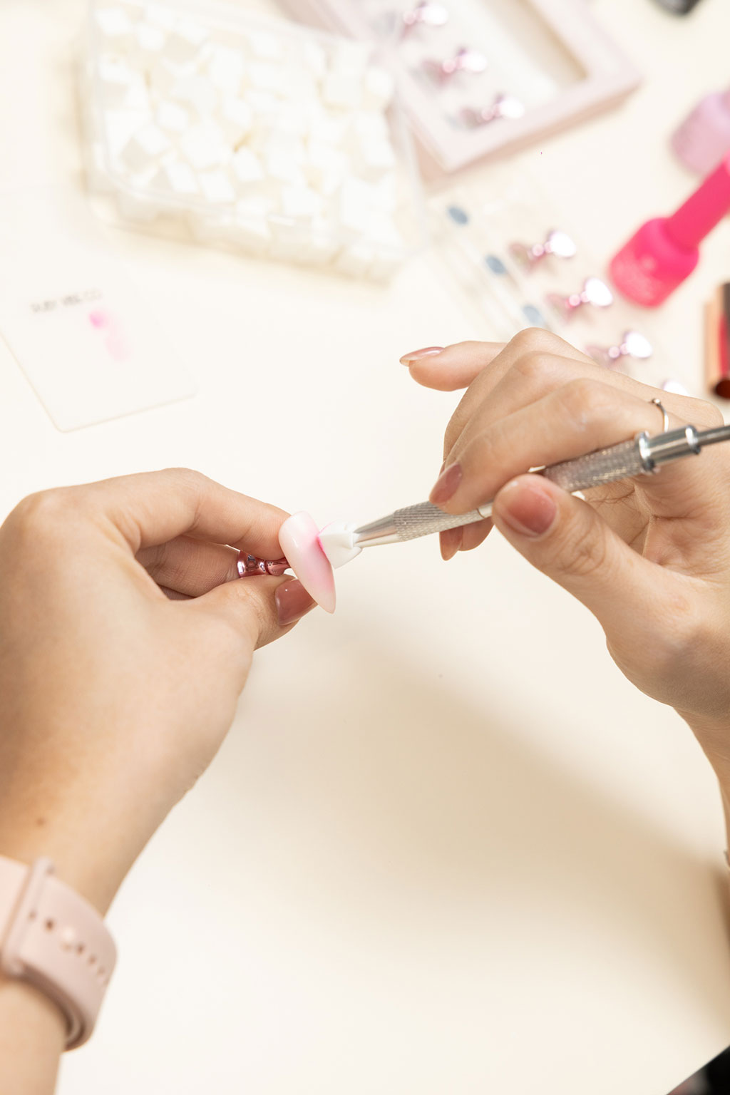 A nail artist's hands using a metal tool to carefully blend the polish on a press-on nail, creating a smooth ombre effect.