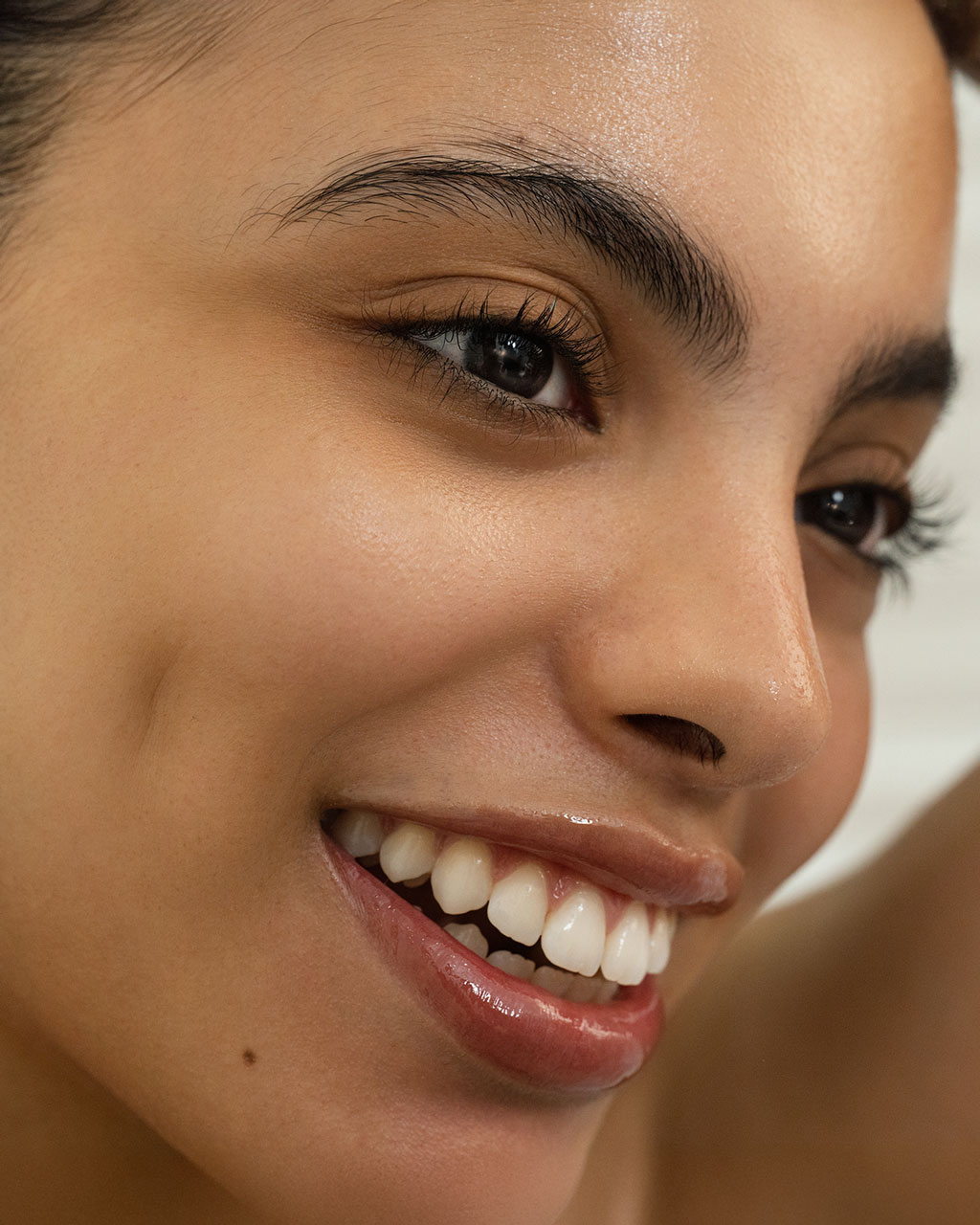 A close-up of a smiling woman with clear, glowing skin and a bright, happy expression.