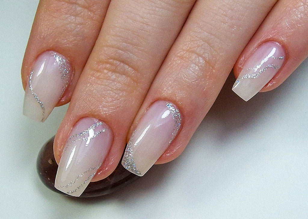 A delicate manicure on long coffin nails, featuring a natural nude ombre base with elegant, sweeping lines of silver glitter.