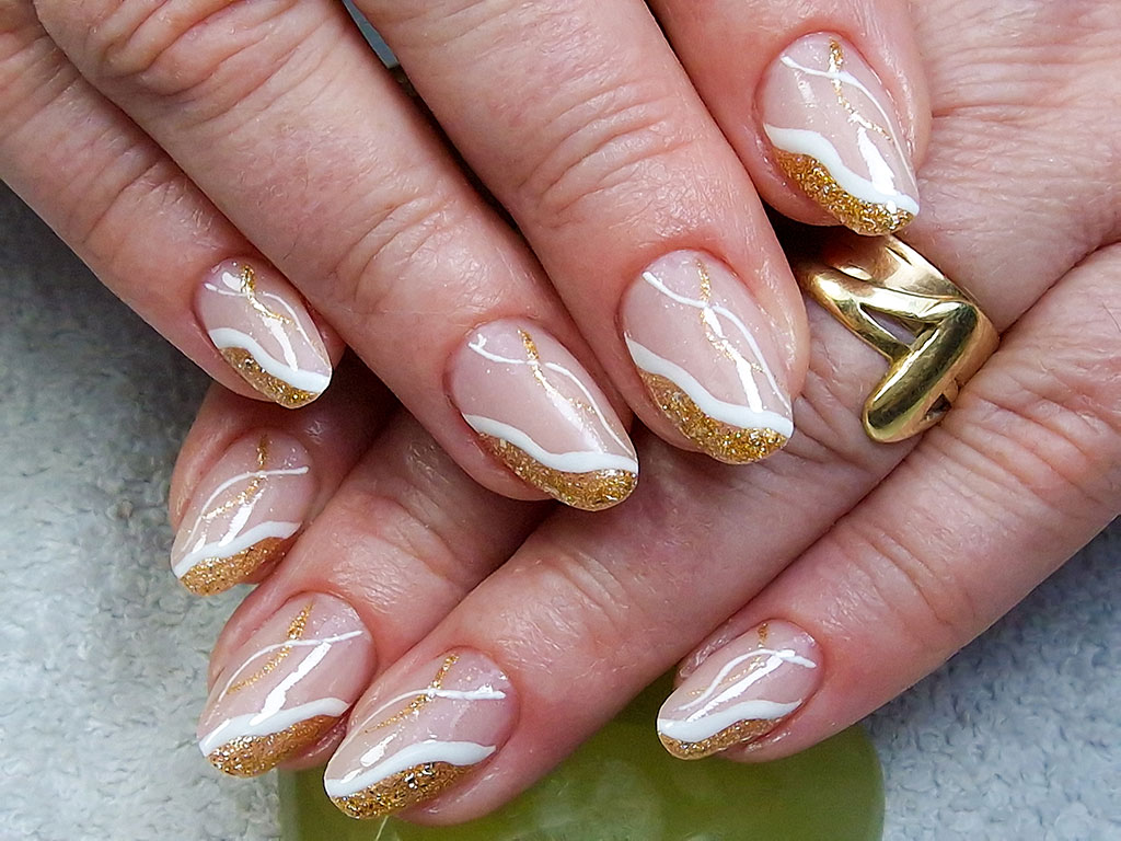 A sophisticated manicure with a sheer nude base, accented with wavy white lines and bold gold glitter tips on almond-shaped nails.