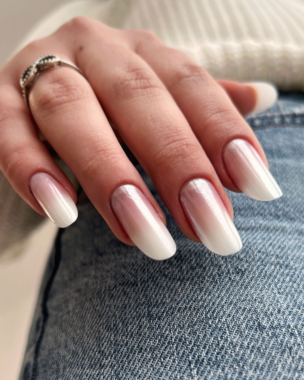 A close-up of a hand with elegant French ombre nails, blending from soft pink to white, resting on blue jeans.