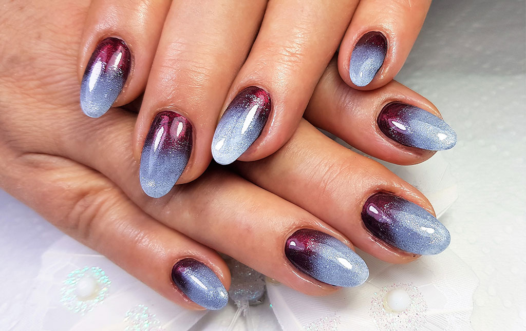 A stunning manicure featuring almond-shaped nails with a glittery ombre effect, transitioning from deep burgundy to a frosty light blue.