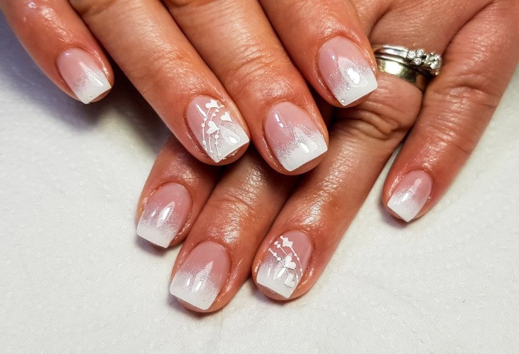 A French ombre, or baby boomer, manicure with silver glitter and delicate white floral art on the accent nails.