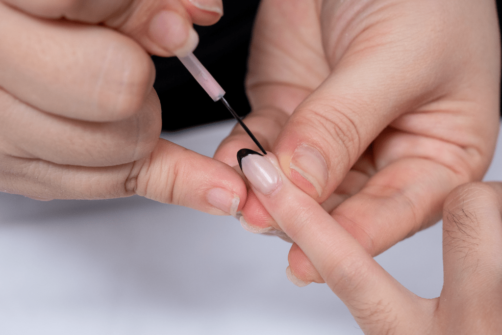 A nail technician using a fine liner brush to carefully paint a black tip for a modern French manicure.