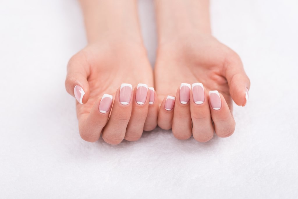 A pair of hands showing a classic and clean French manicure on perfectly shaped, medium-length square nails against a white background.