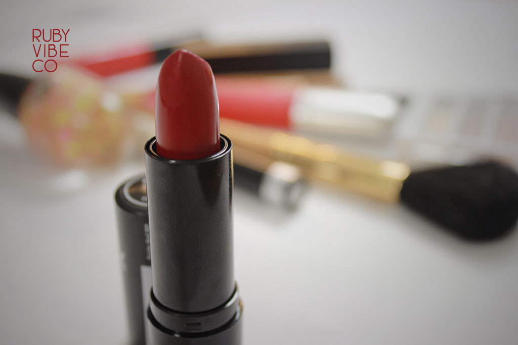 A close-up of a new red lipstick in a gold tube.