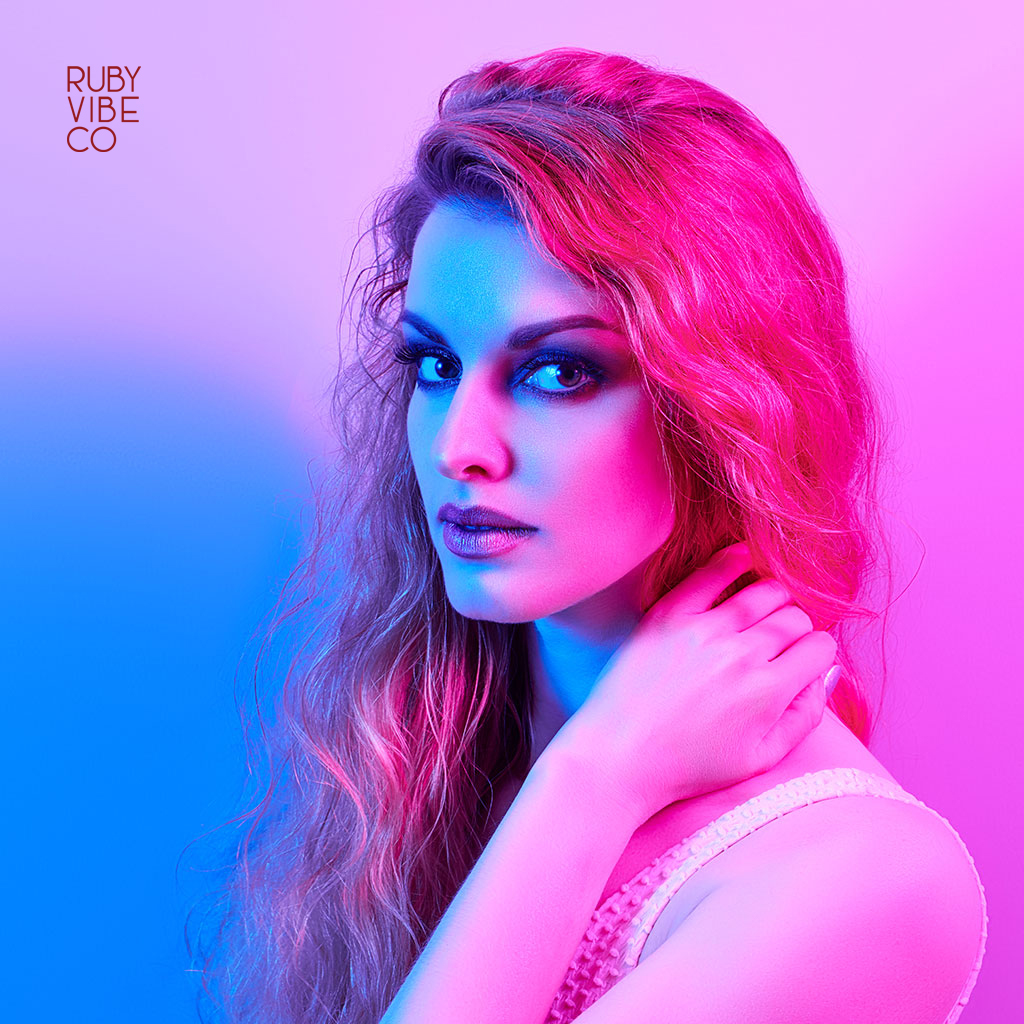 A woman with dramatic makeup under vibrant pink and blue studio lighting.