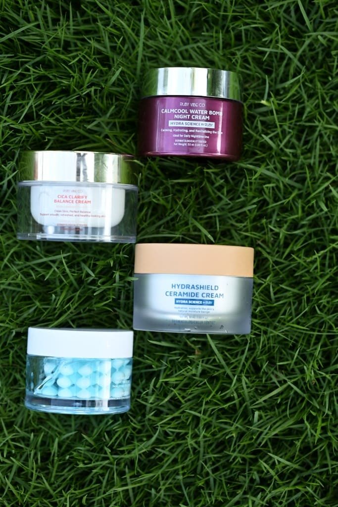 An overhead shot of four different jars of face cream arranged in a grid pattern on a lush green lawn. 