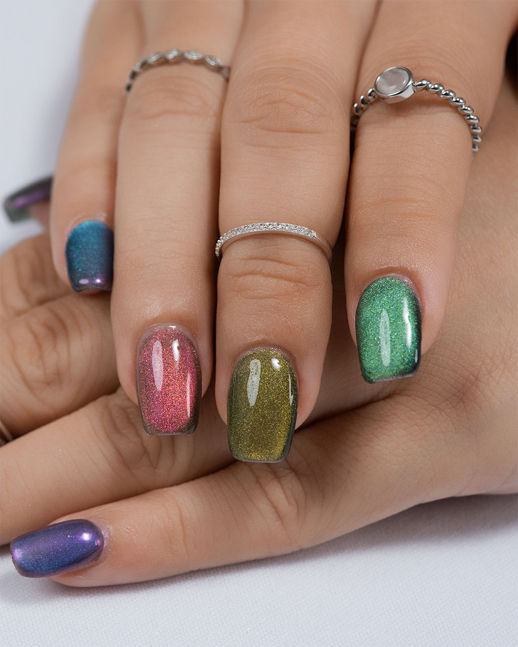 A colorful cat-eye manicure with each nail painted a different vibrant shade, including green, pink, blue, and purple.