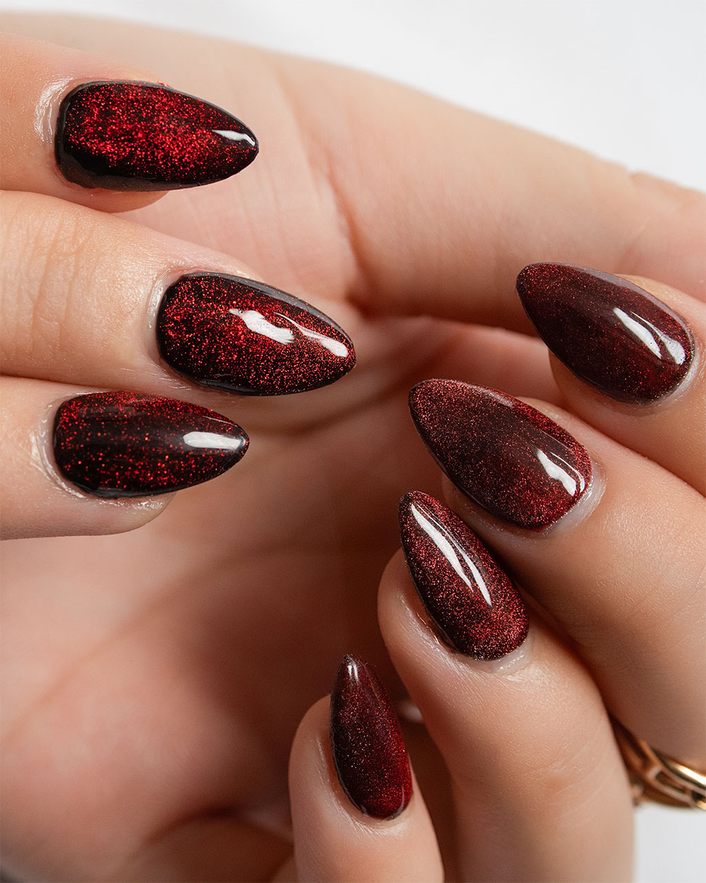 A close-up of a glamorous manicure featuring long, almond-shaped nails with a sparkling deep red cat-eye polish.