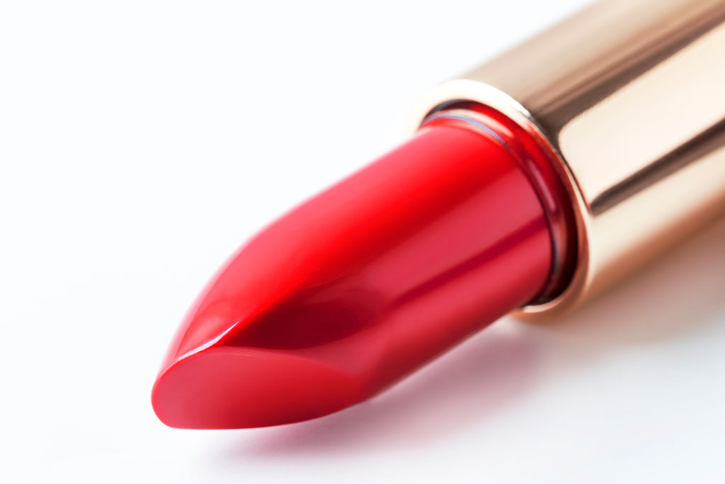 A close-up of a new red lipstick in a gold tube.