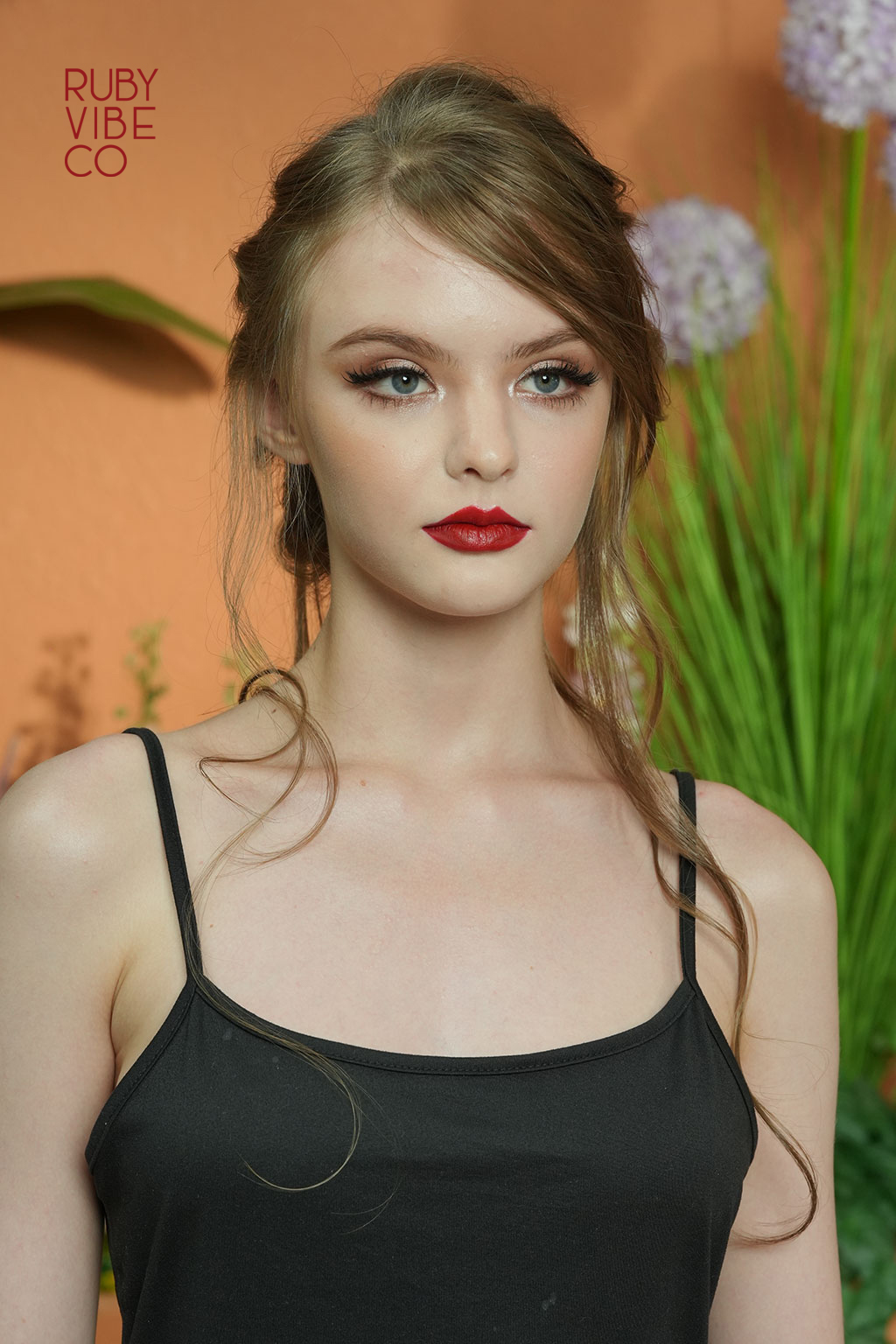 Close-up of a vibrant red lipstick in a gold tube against a plain white background.