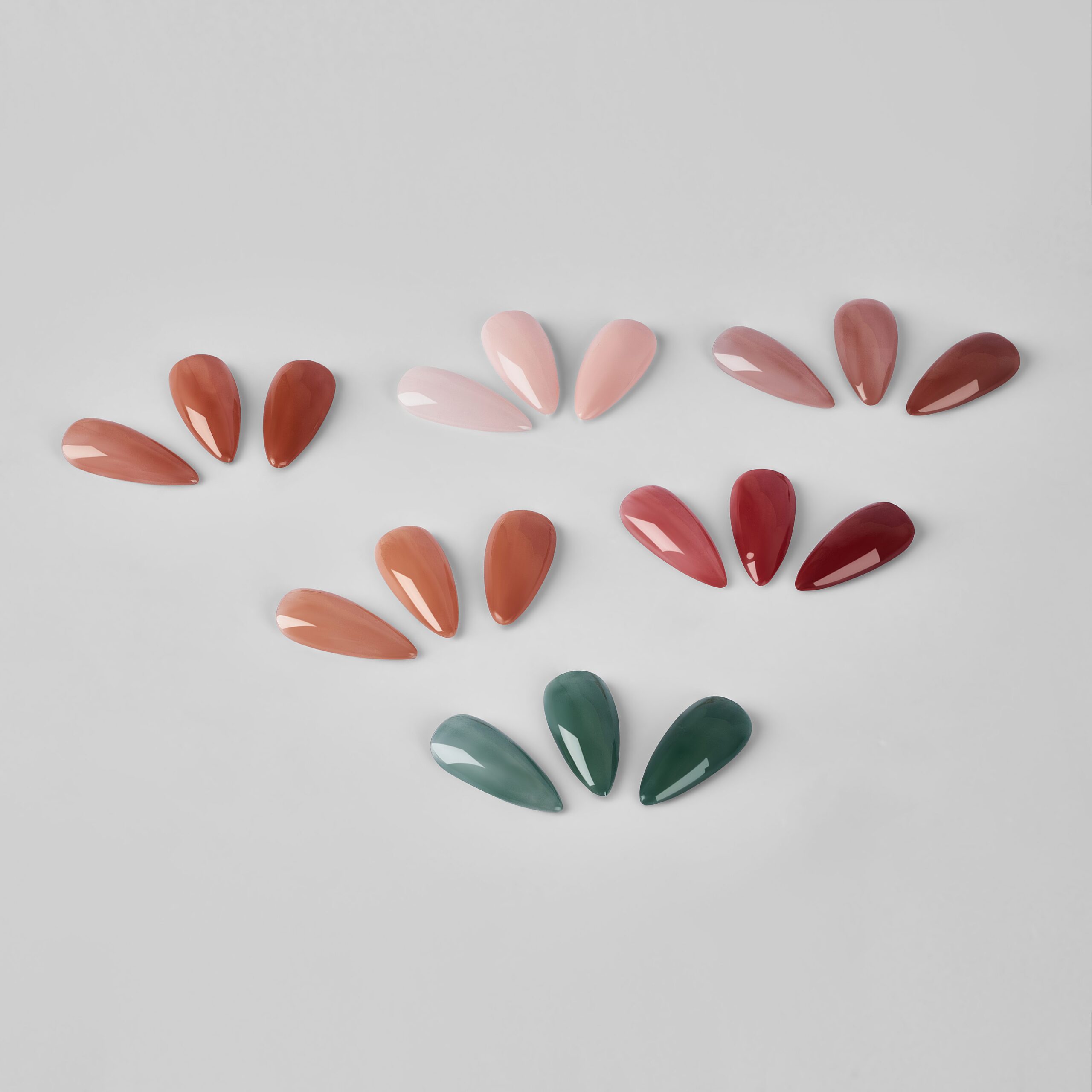 A collection of artificial nails fanned out in groups, showcasing a variety of beautiful autumn nail colors including earthy browns, soft pinks, deep reds, and forest greens. This image provides a guide to the best fall nail colors for a chic manicure.
