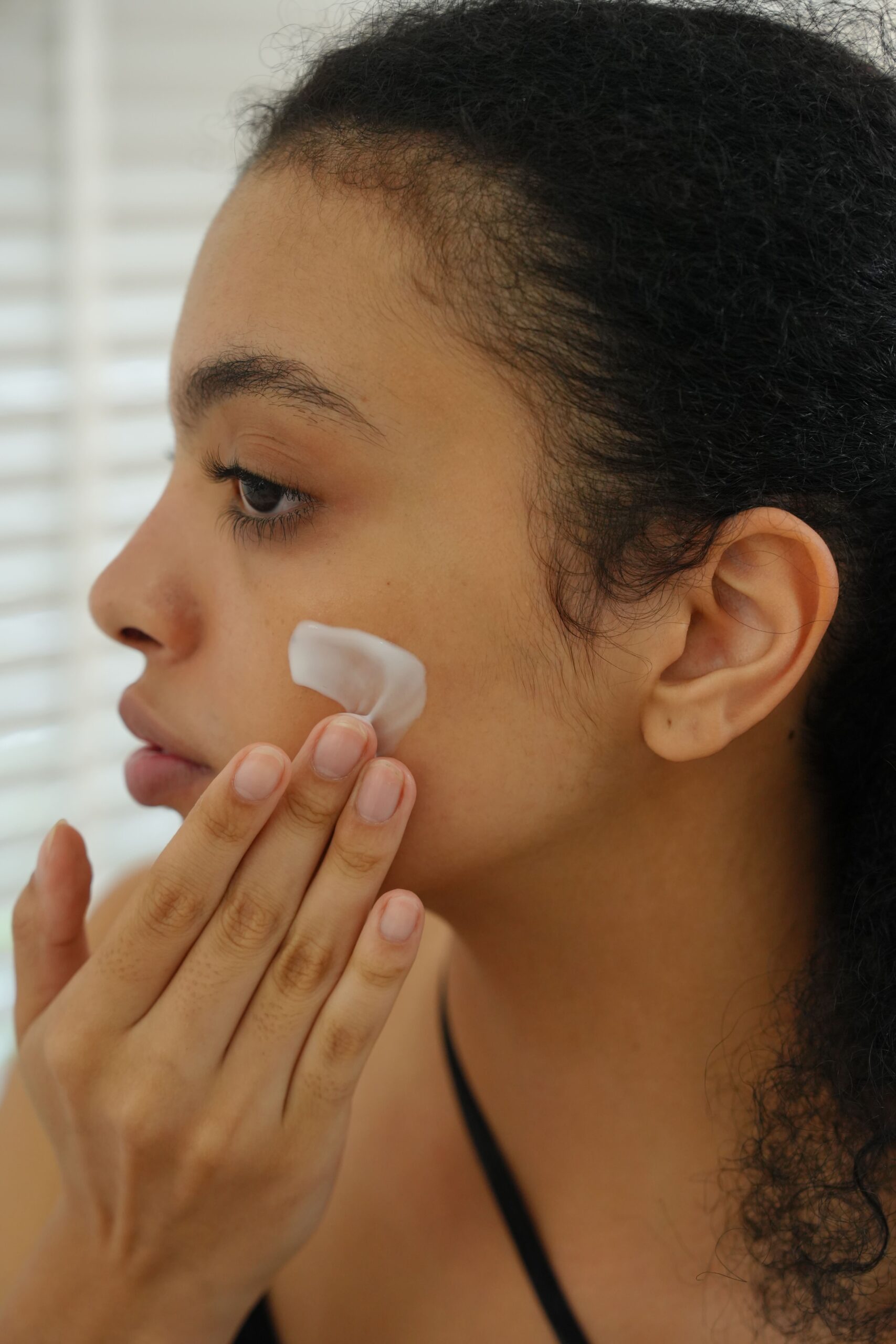 A person applies a white moisturizer to their cheek, showcasing the proper use of a product formulated with key ingredients for oily skin.