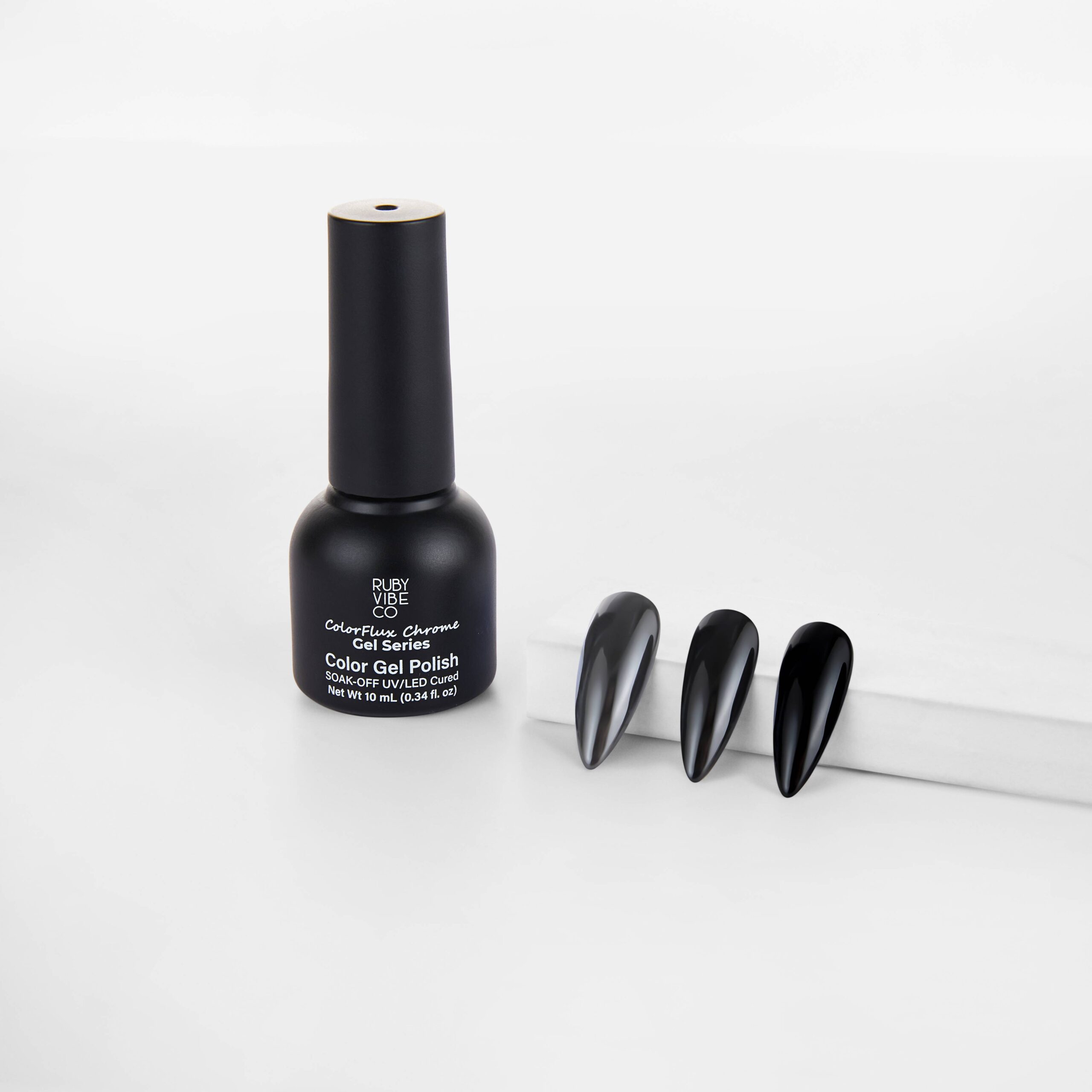 A sleek black bottle of Ruby Vibe ColorFlux Chrome Gel Polish standing next to three long, coffin-shaped nail tips with a deep black, mirror-like chrome finish.