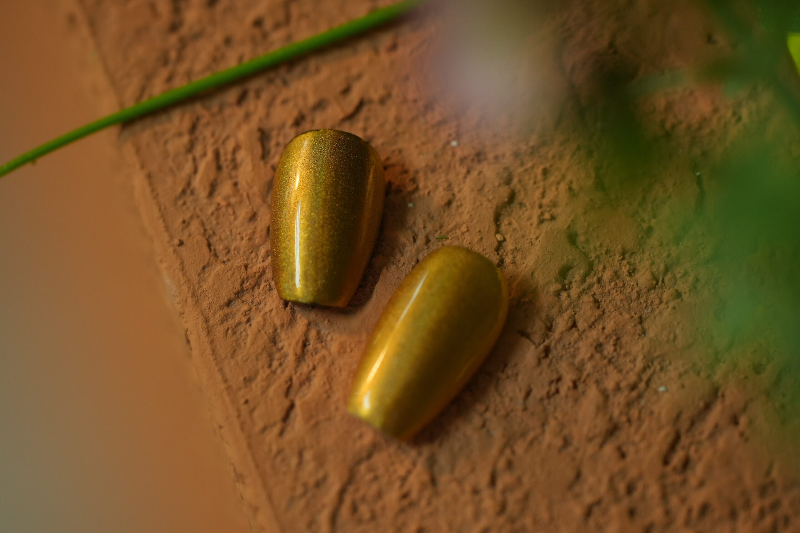 Two finished, coffin-shaped nail tips with a shimmering Yellow chrome effect, demonstrating a smooth, reflective surface.