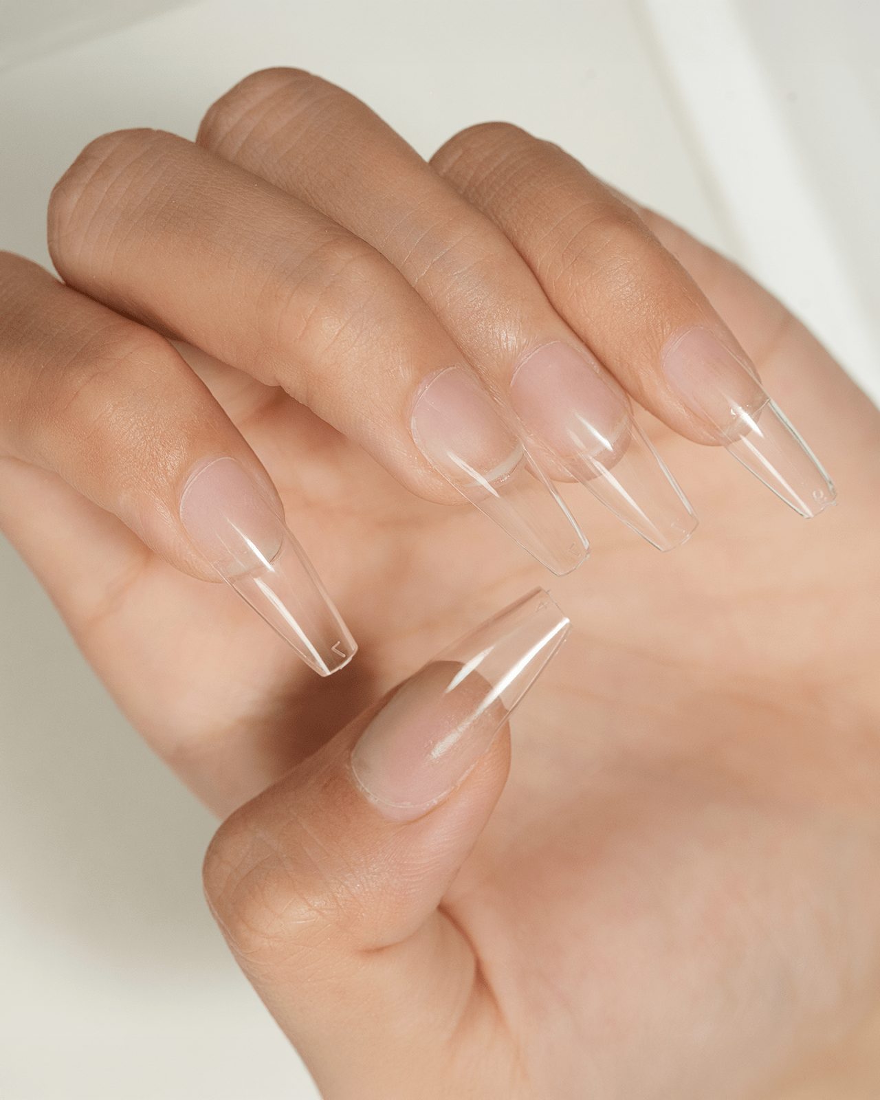 A hand with perfectly applied clear, long, coffin-shaped artificial nail tips. This image illustrates the first step of a DIY manicure, showing how to prepare the base for a cozy fall nail design at home.