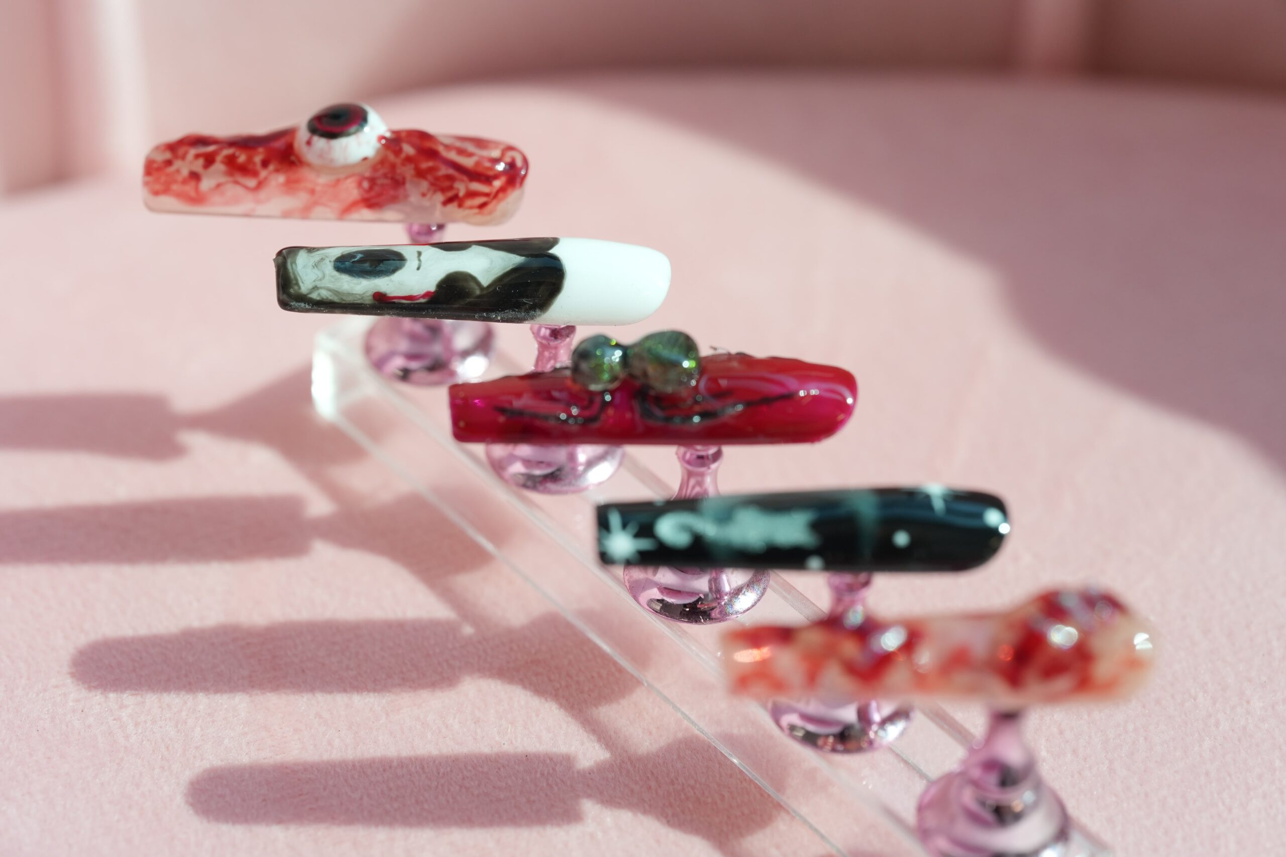 A set of five different false nails on stands, showcasing a variety of spooky Halloween designs including a bloody eye and a ghost.