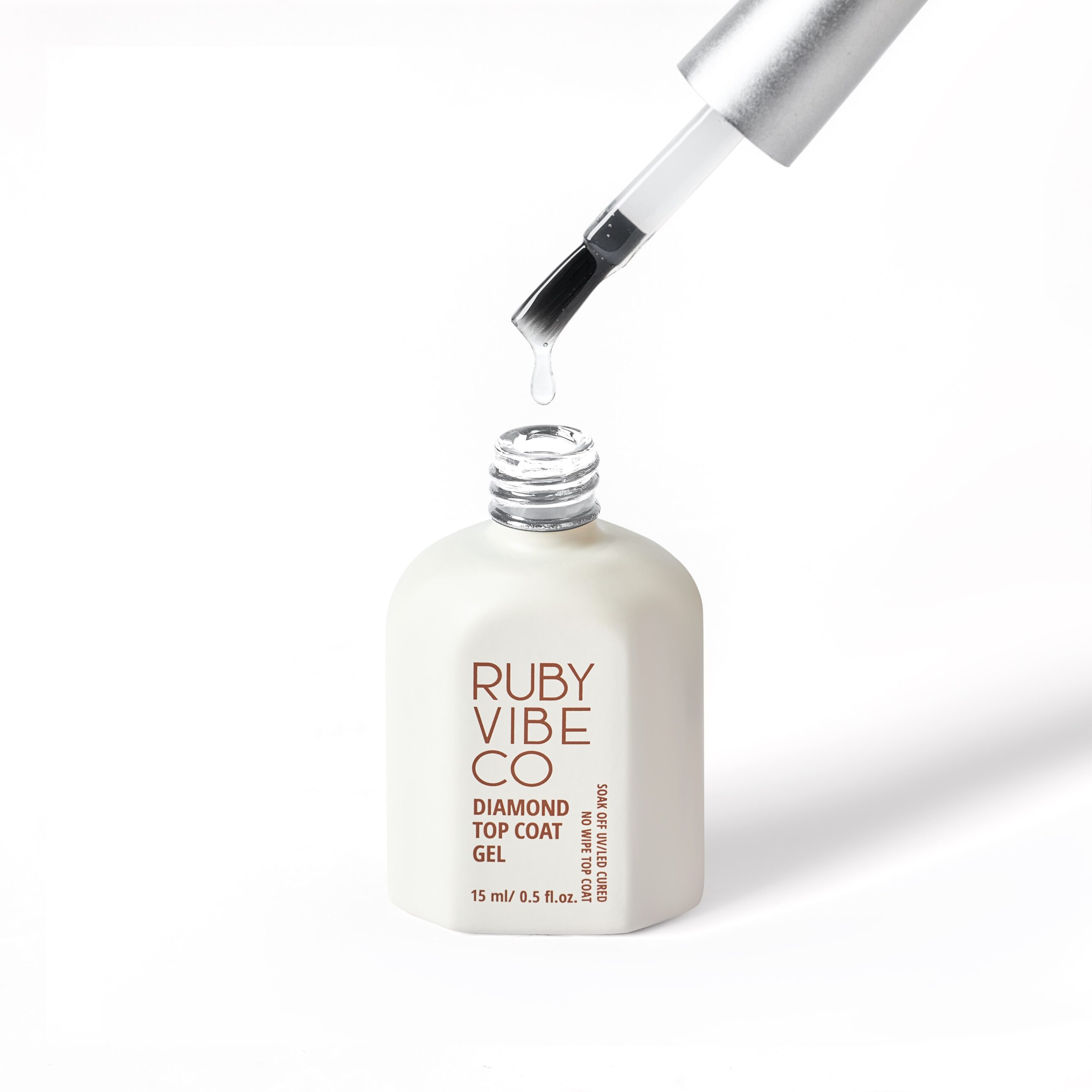 DIY Halloween Nails: A clear bottle of Ruby Vibe Co. Diamond Top Coat Gel. The brush, held above the bottle, has a drop of gel on its tip, illustrating the final step of a gel manicure for adding shine and durability to your spooky Halloween nail designs.