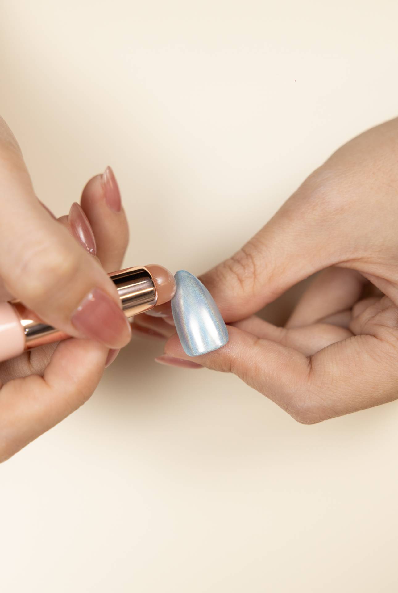 A close-up shot of a hand applying a chrome powder pen to a nail tip, showing the a vibrant, mirror-like finish.