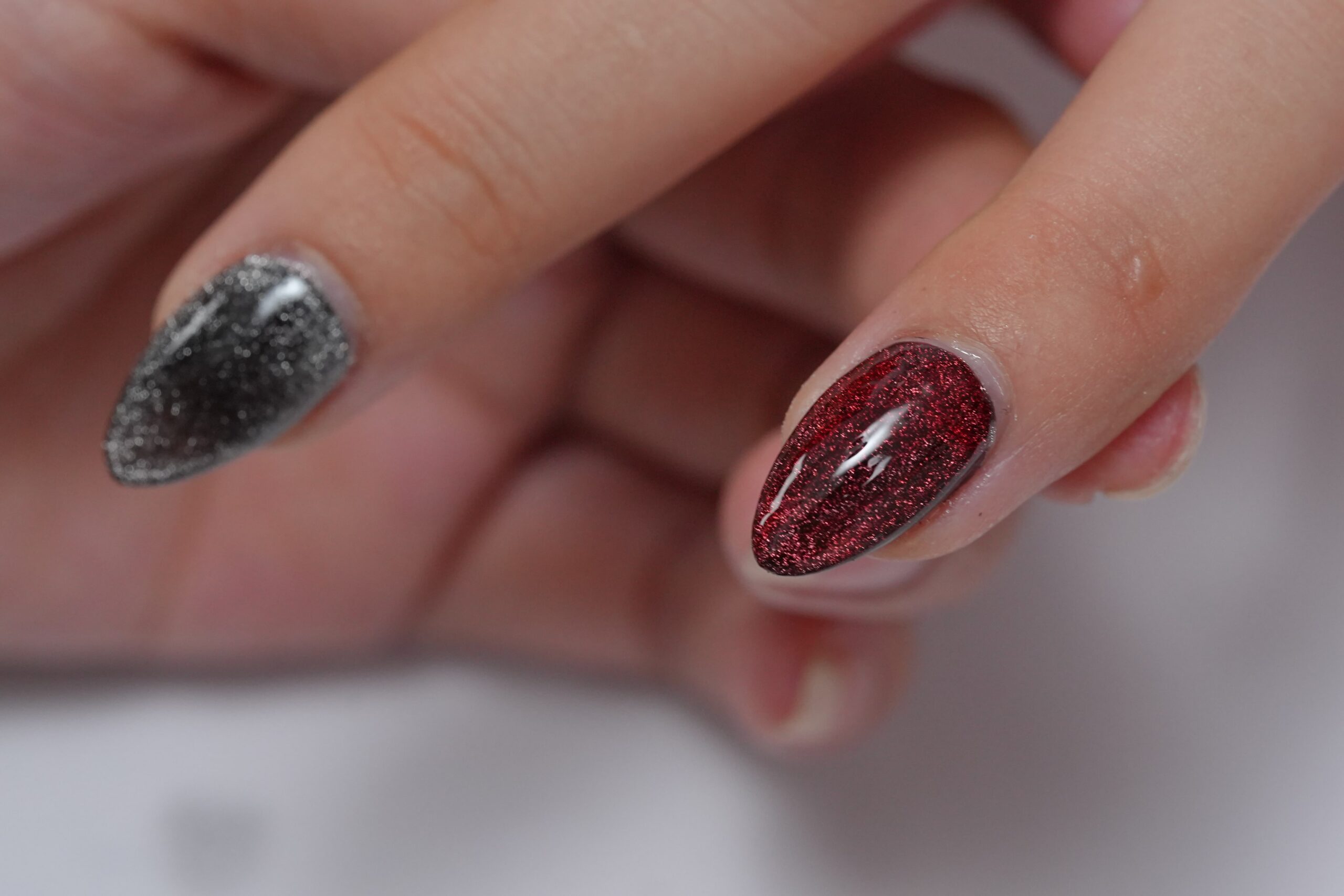 Halloween Nail Art: A close-up of two fingers showing off glitter gel polish. One nail is a shimmering deep red and the other is a sparkling dark gray, demonstrating a glamorous and spooky color combination perfect for a chic Halloween look.