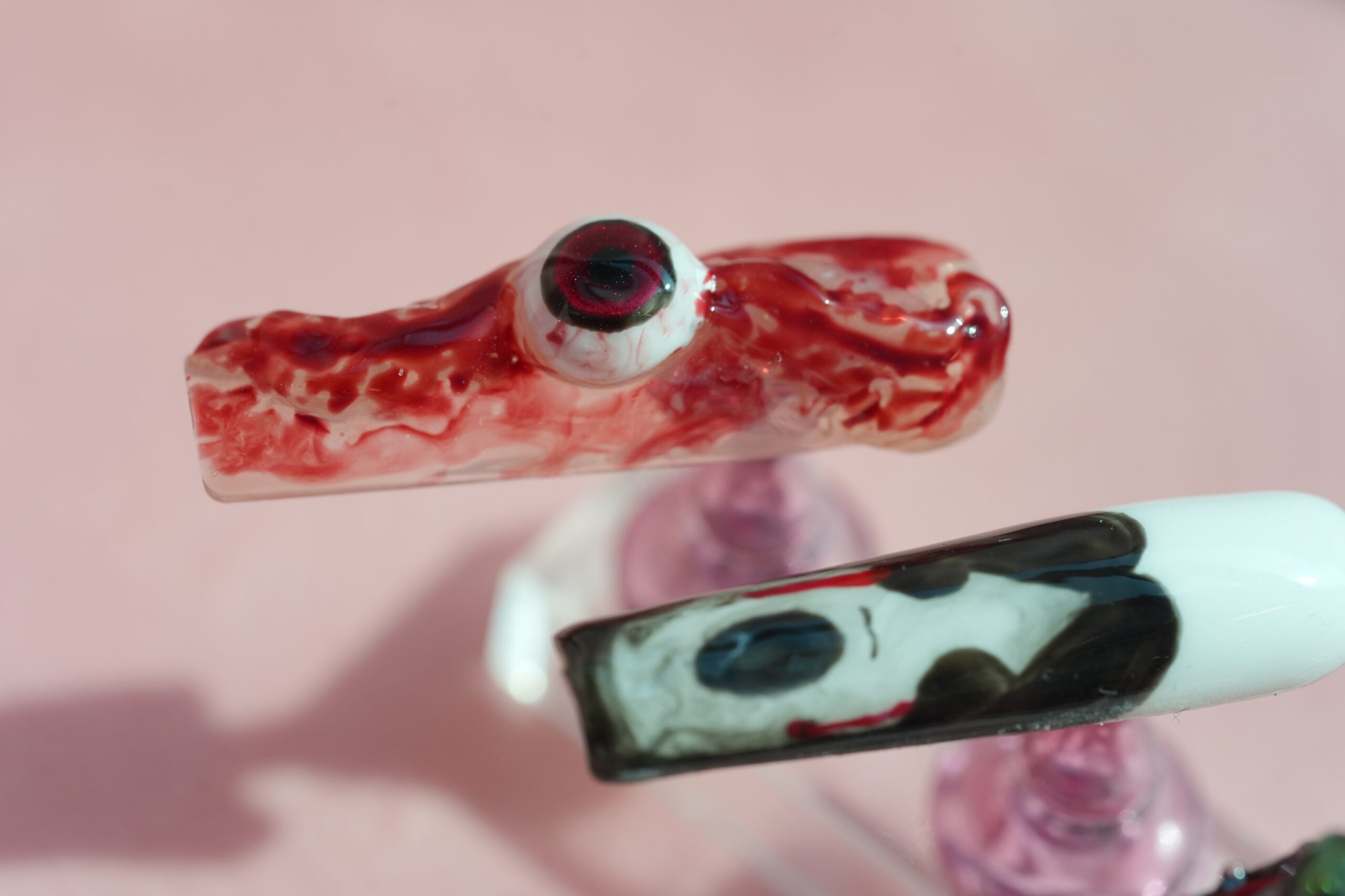 Halloween Nail Art: An artificial nail with a chilling eyeball and blood drip design is placed next to another nail with an abstract black and white pattern. The image captures gory and macabre nail art ideas, perfect for a truly spooky Halloween look.