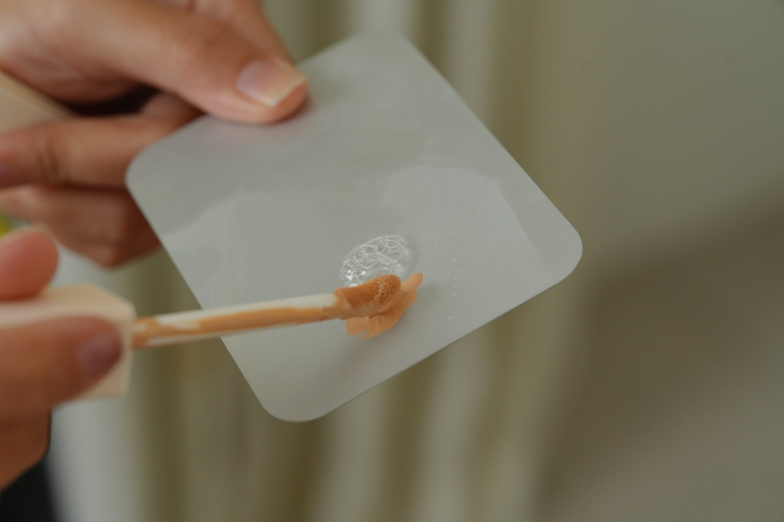 A hand dabs a peach-toned color corrector onto a makeup palette, demonstrating a key step in concealing dark circles.