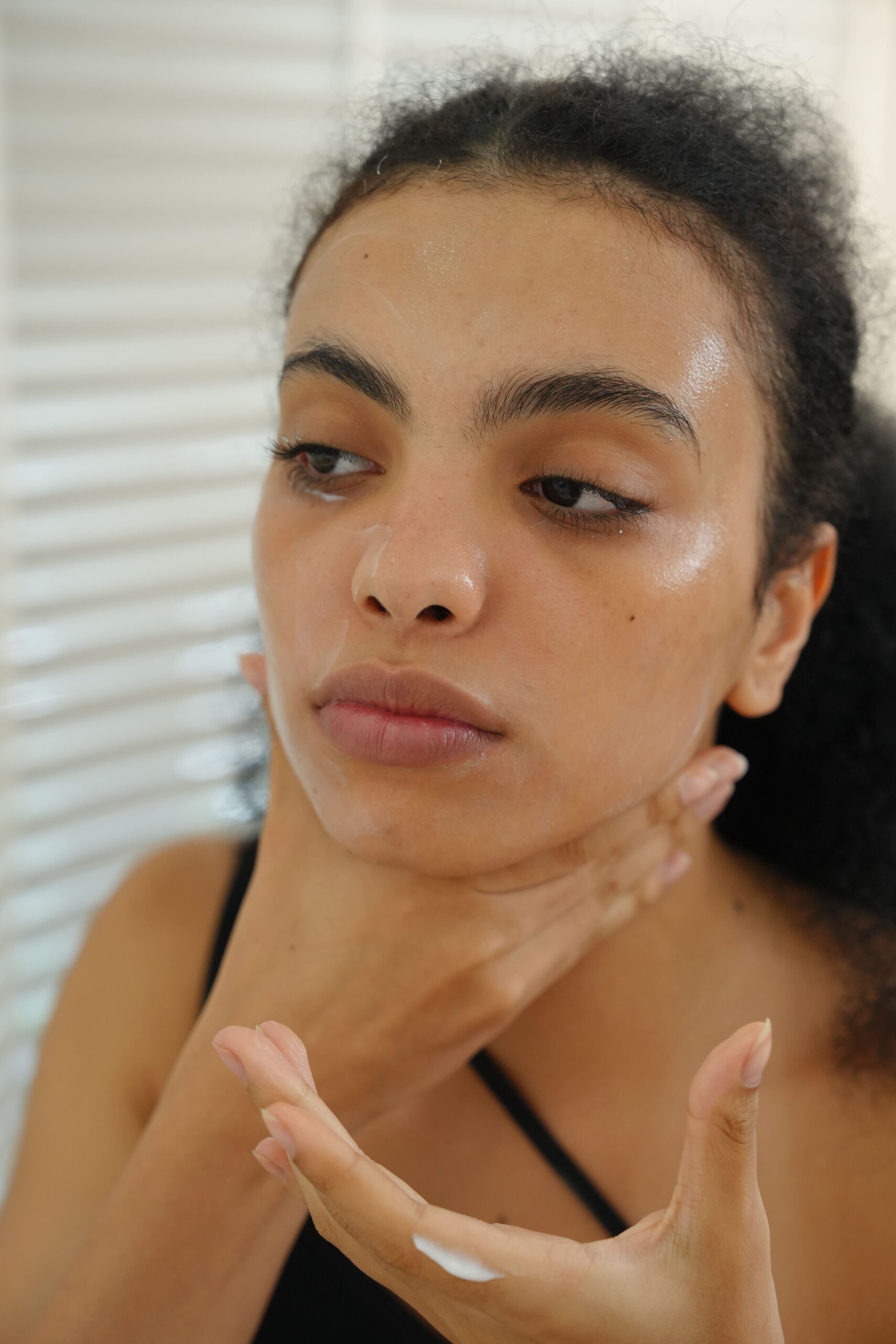 A person applies a moisturizer to her face and neck, demonstrating the essential skincare step before applying makeup to conceal dark circles.