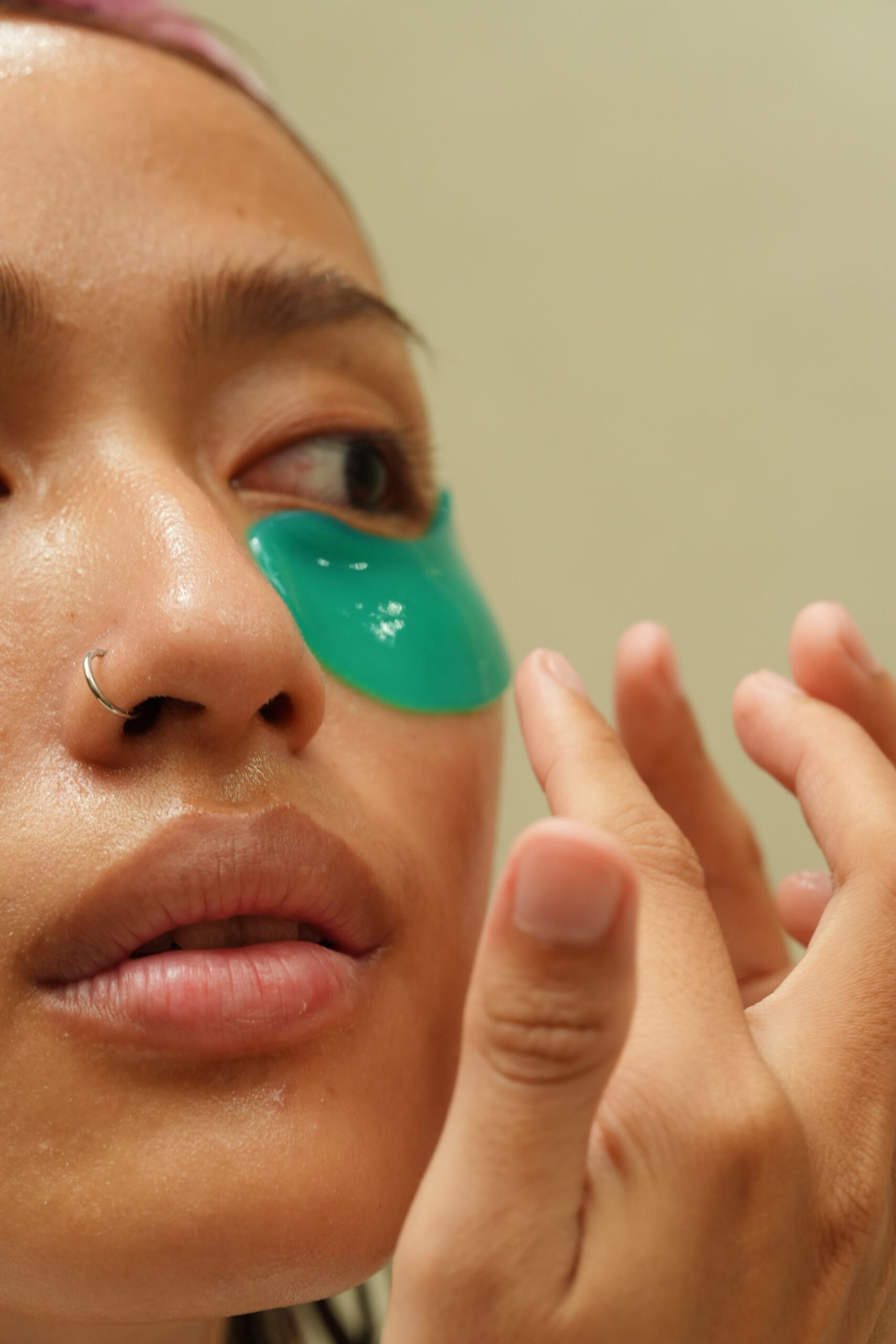 A person applies a green gel eye patch under their eye, demonstrating a relaxing and hydrating step in a routine to get rid of dark circles.