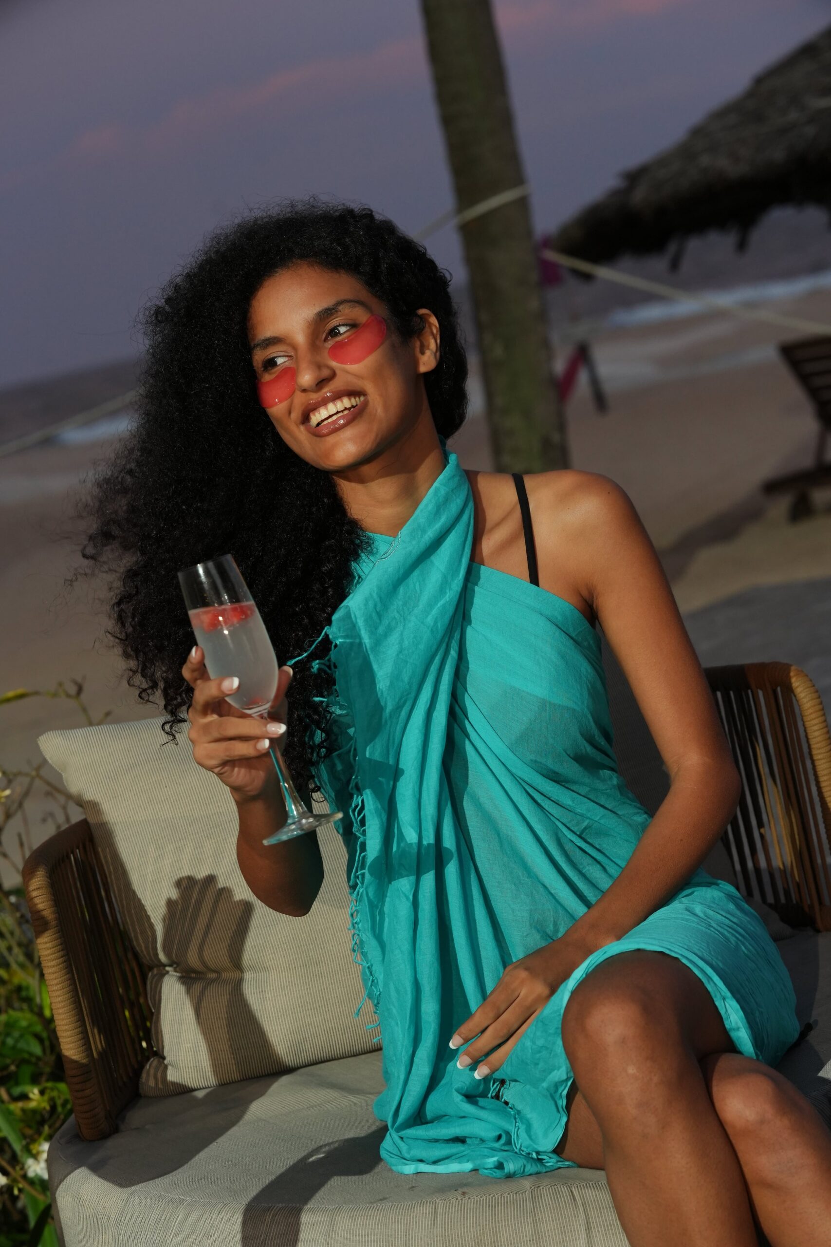 A woman with under-eye patches smiles while relaxing outdoors, representing the importance of stress reduction and self-care in managing acne breakouts.
