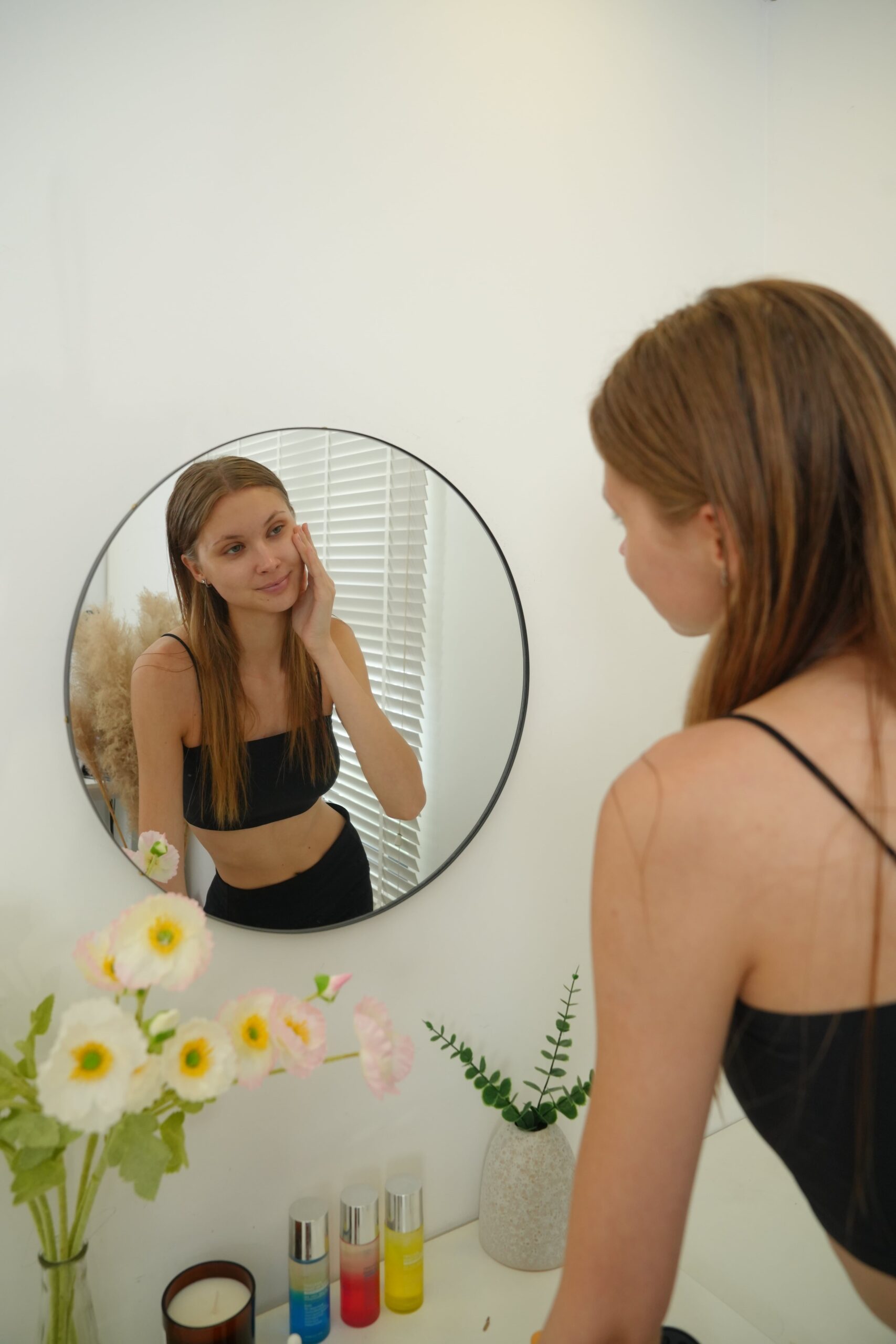 A person looks at their reflection in a mirror while touching their face, representing the self-care ritual of a daily skincare routine for dark circles.