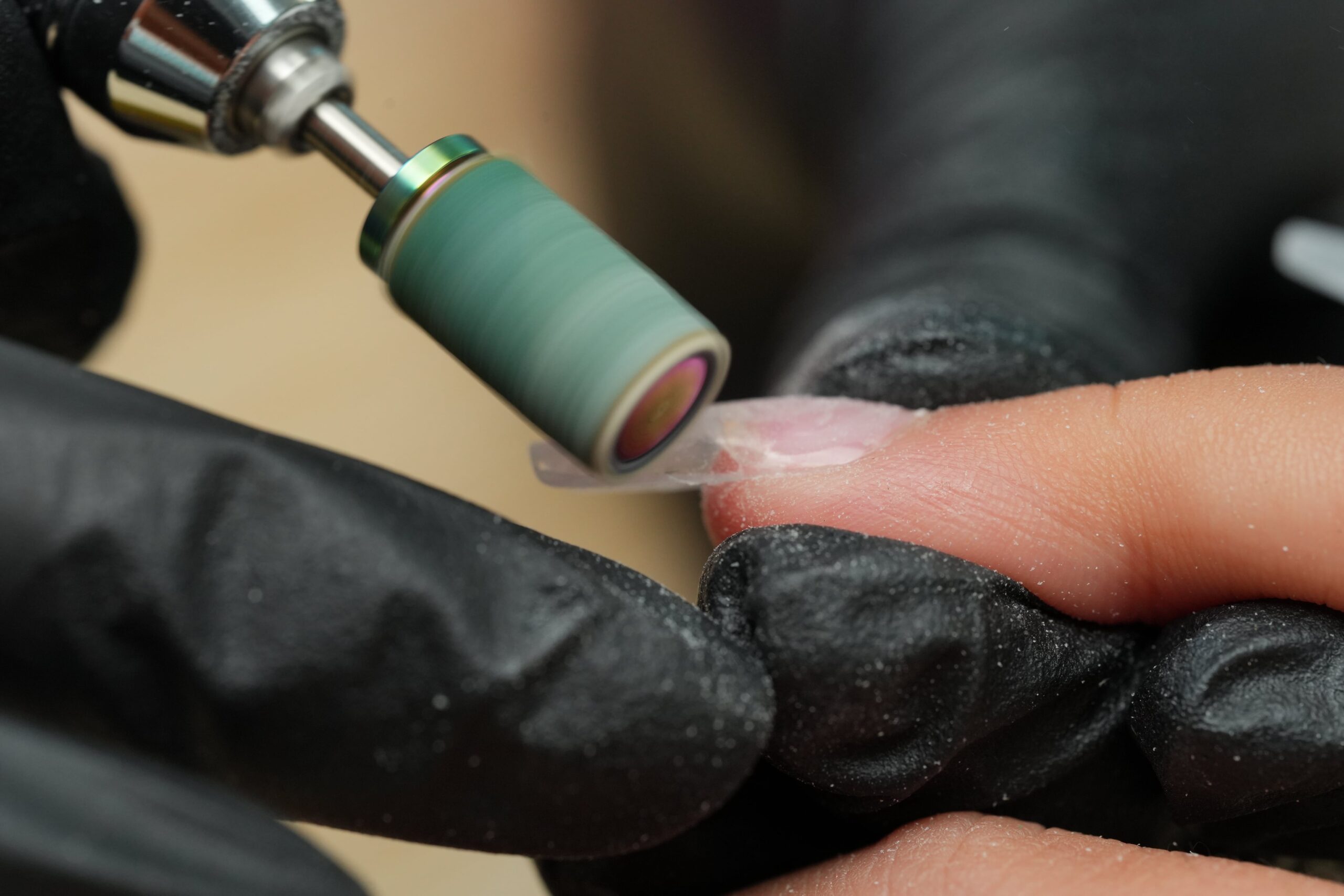 A nail technician, wearing black gloves, uses an electric file to shape and smooth an artificial nail. This is an essential tip for proper nail preparation, ensuring a strong and long-lasting spooky Halloween manicure.