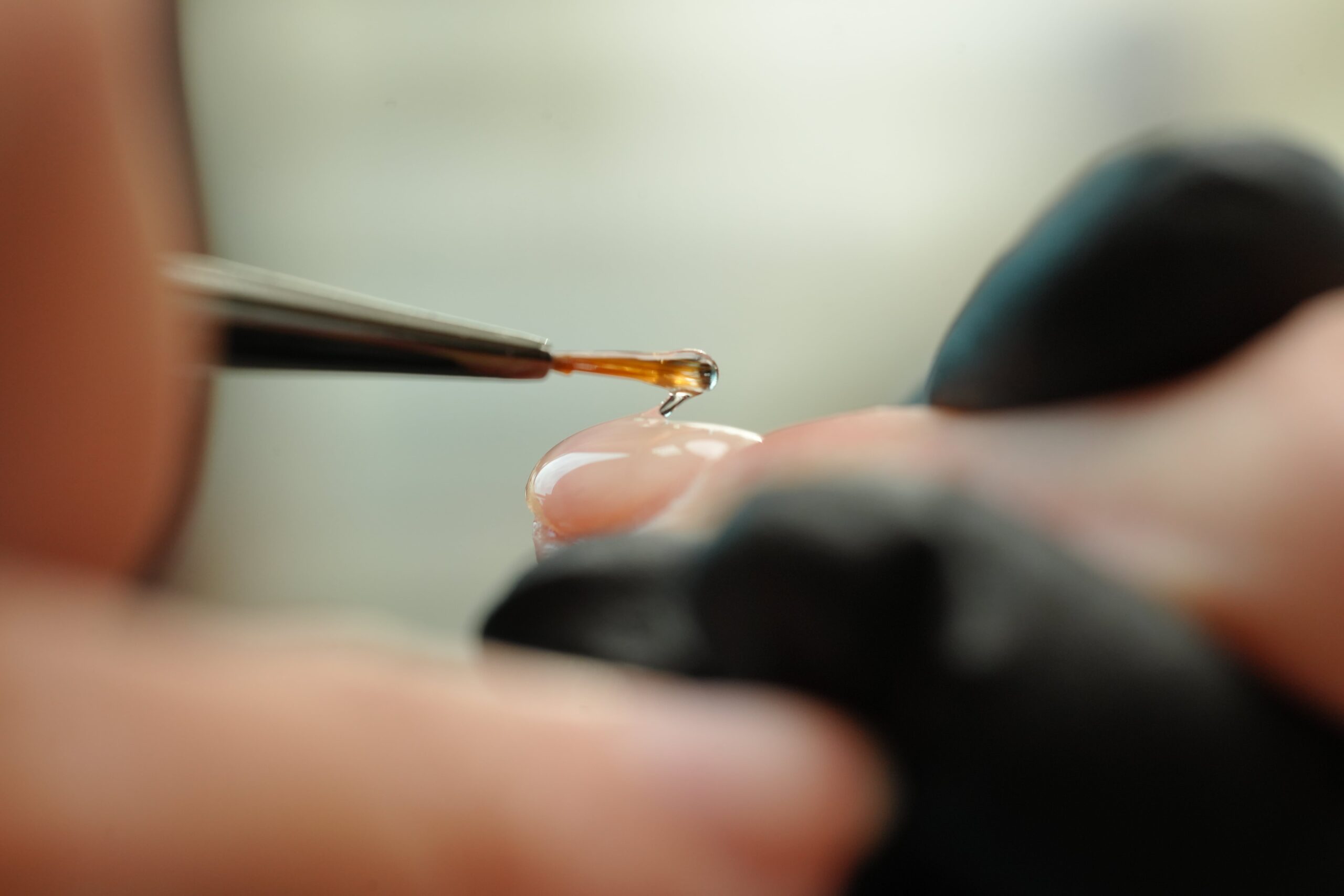 A gloved hand uses a brush to apply a drop of gel adhesive onto an artificial nail. This is a crucial tip and trick for securely attaching nail art embellishments, ensuring gems or other spooky decorations stay put on your Halloween manicure.
