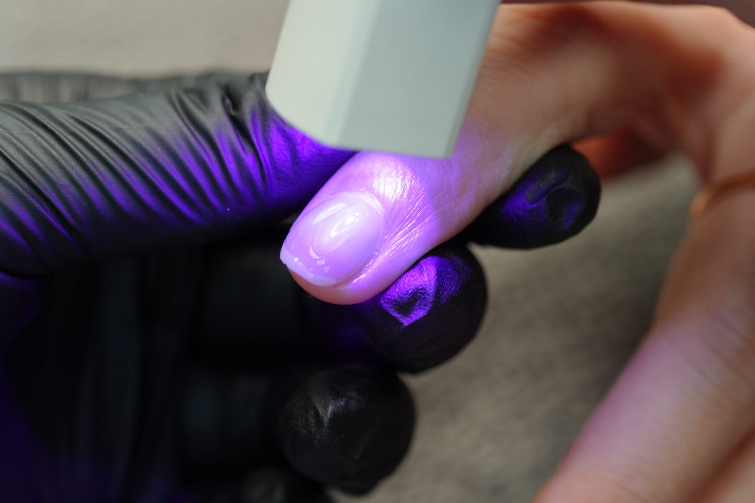 DIY chrome nails: Curing the base gel layer on a natural nail using a UV lamp for durability.