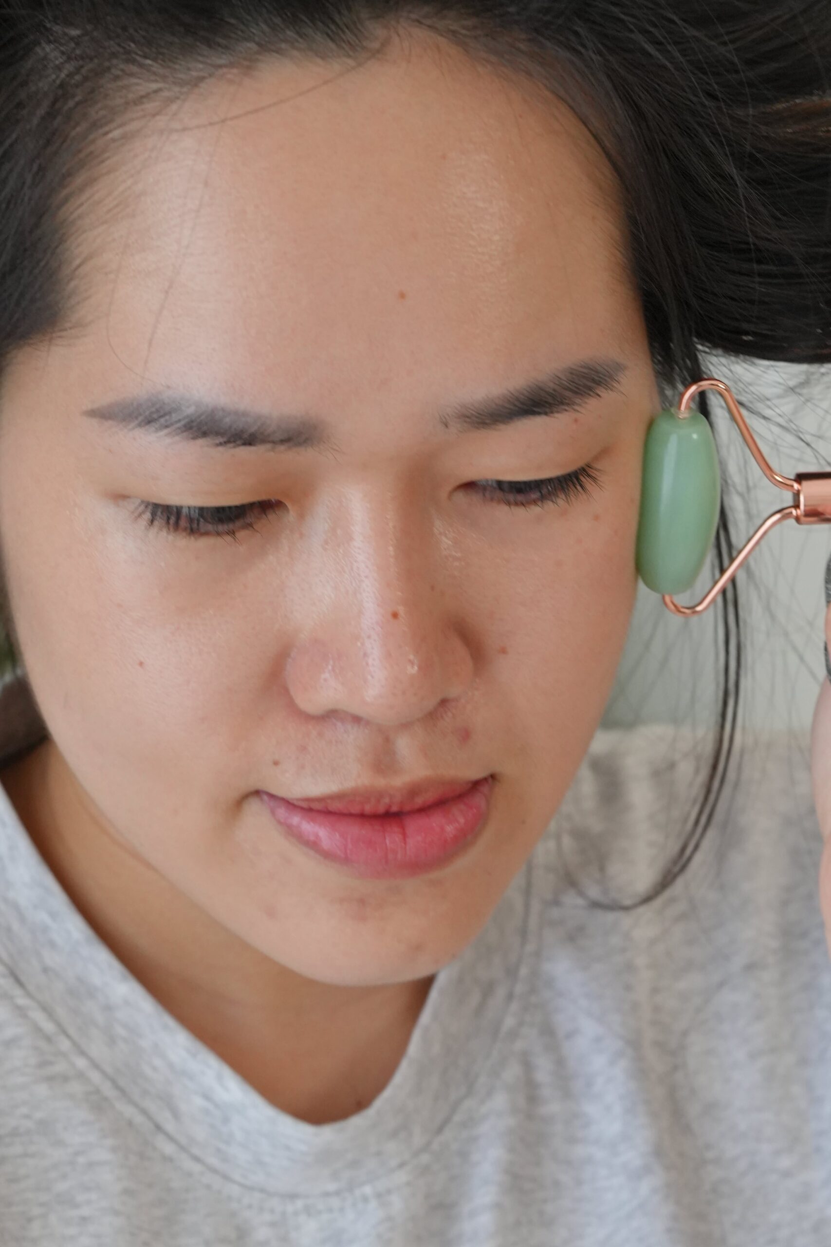 A person uses a jade roller on their face, highlighting a tool often used in a skincare routine to improve product absorption and lymphatic drainage.