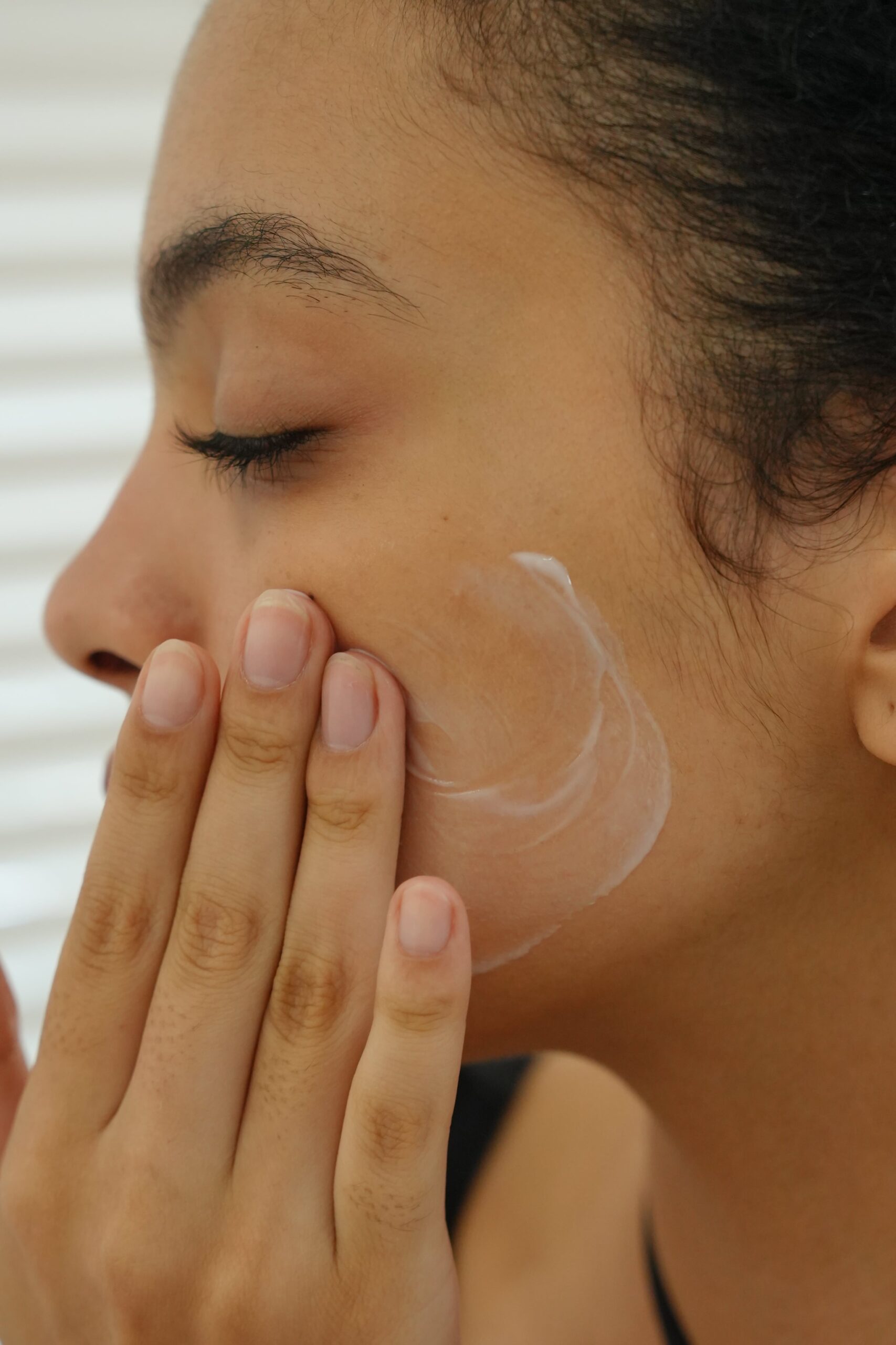 A close-up of a hand gently massaging a white cream onto a person's cheek, debunking the myth that oily skin doesn't need moisturizer.