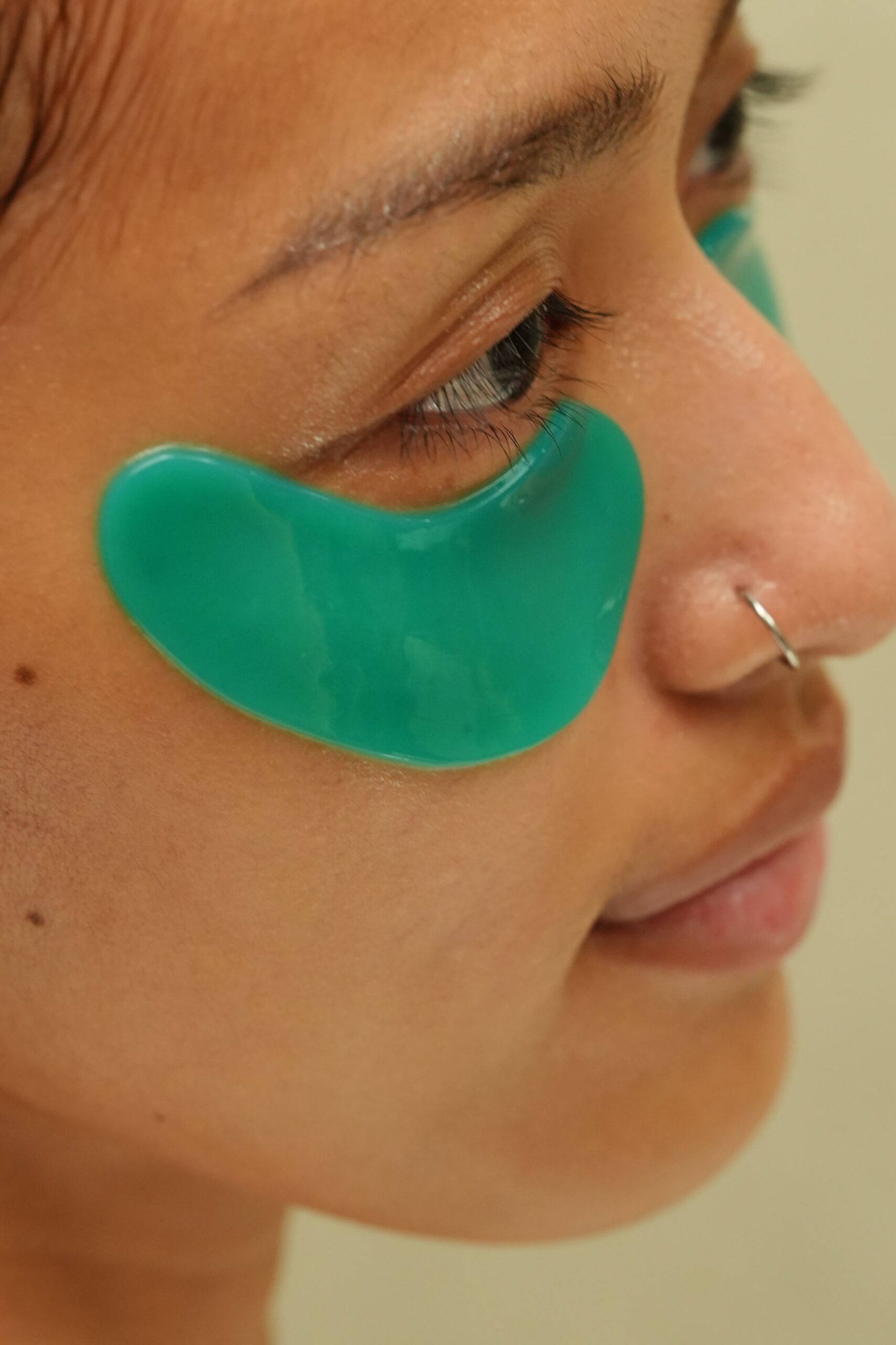 A close-up of a person wearing green gel eye patches, demonstrating a treatment step in a skincare guide to get rid of dark circles.