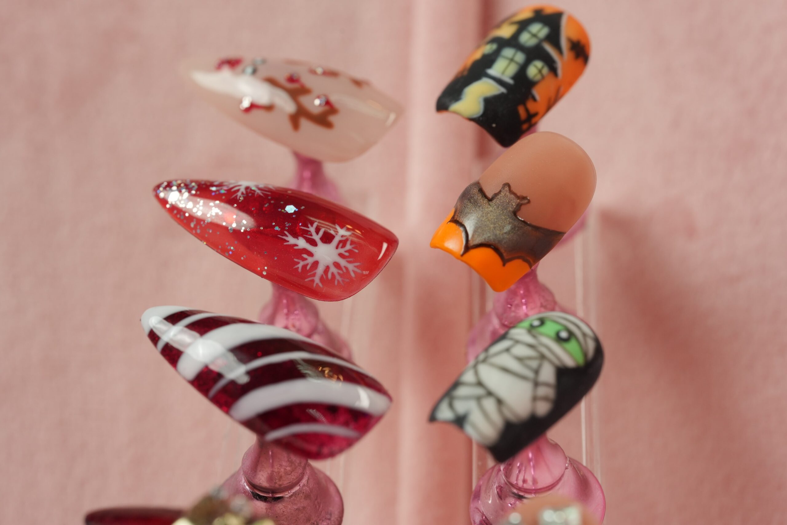 A collection of various Halloween and holiday-themed nail art designs on display, including a mummy, haunted house, glitter snowflake, and candy cane stripes, showcasing creative options for frightfully fun nail designs.