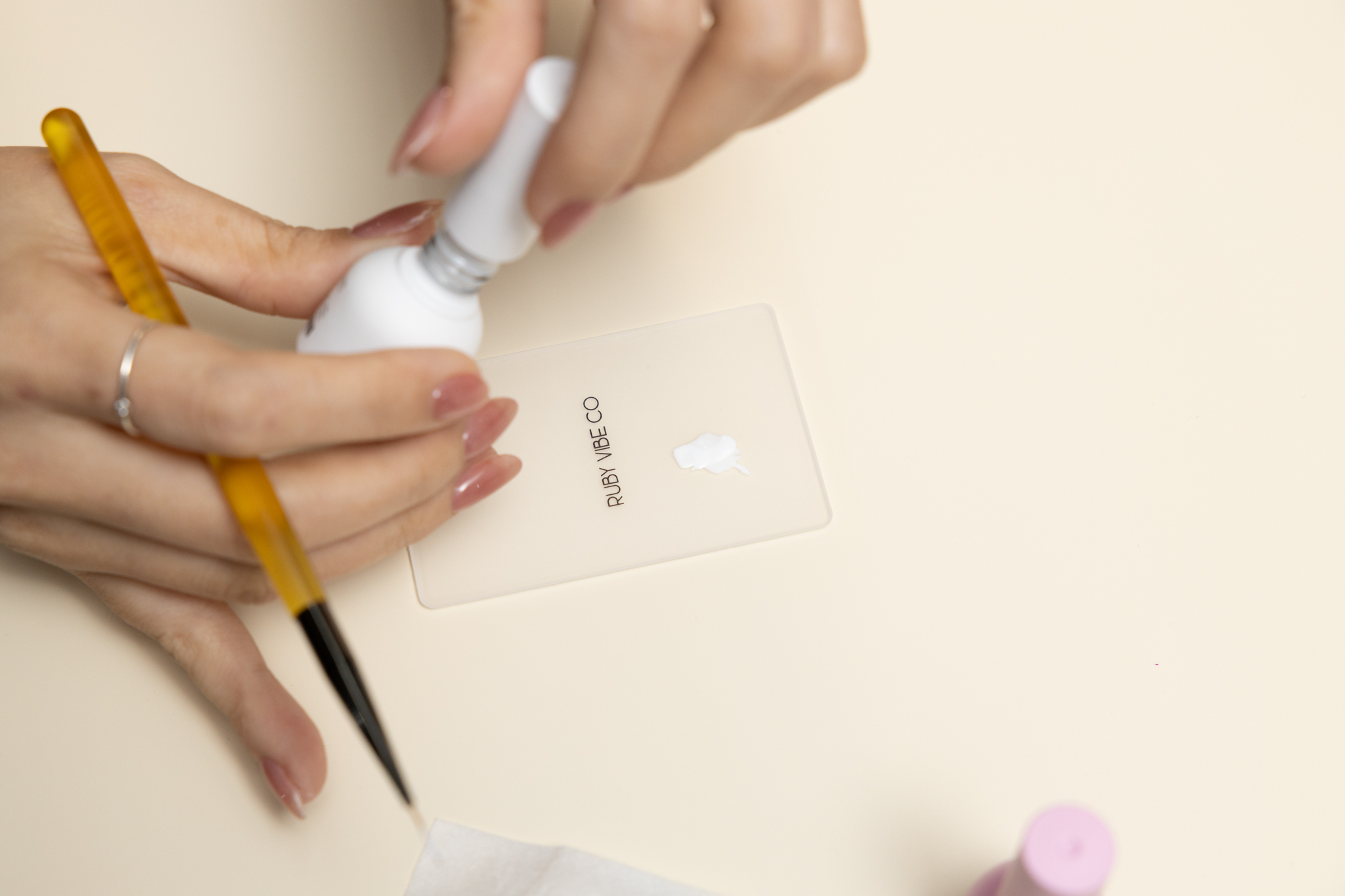 A manicurist's hands preparing to create Halloween nail art, holding a bottle of white nail polish over a palette with the Ruby Vibe Co. logo.