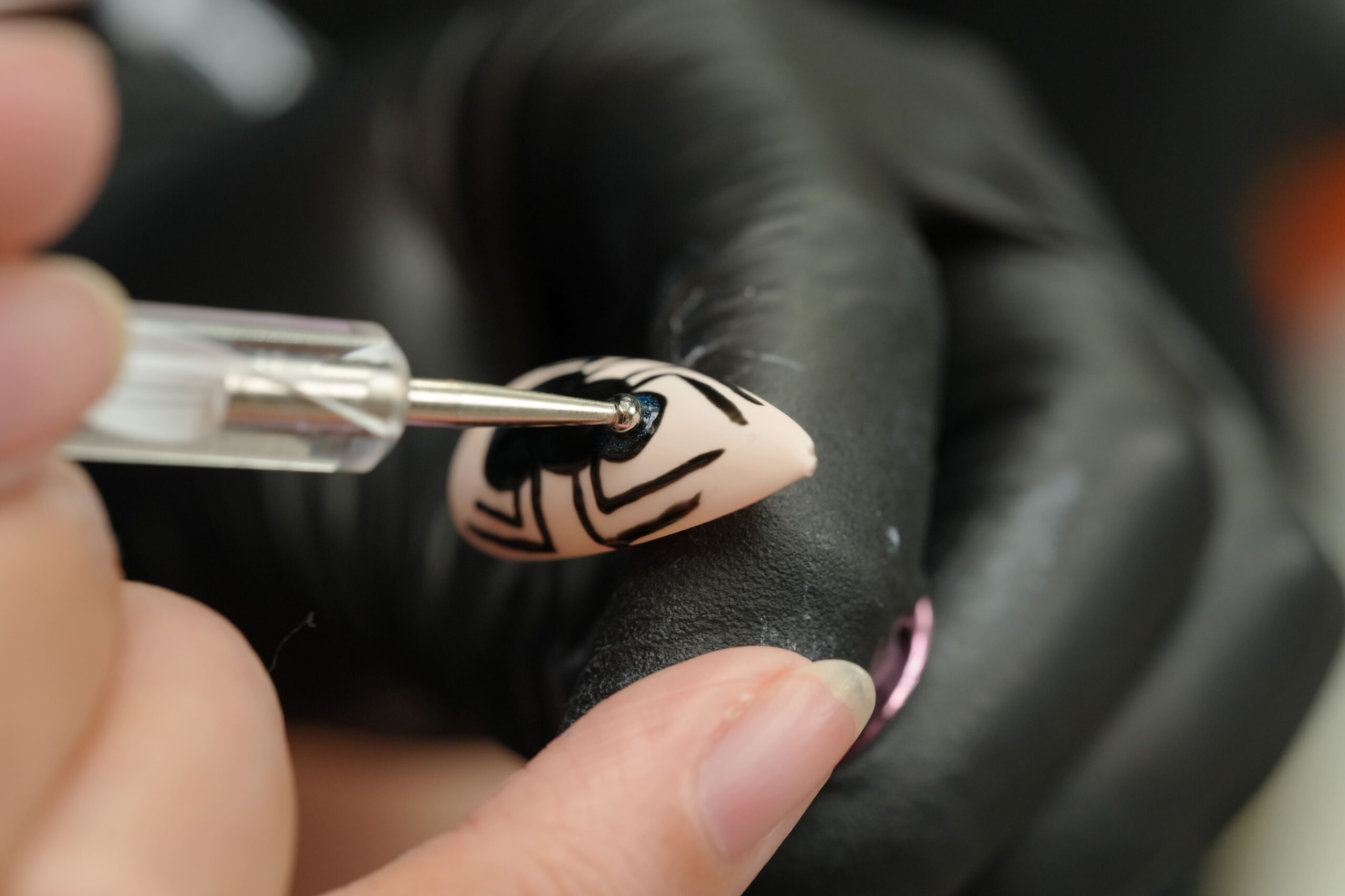 An artist using a dotting tool to carefully apply glitter detail to the body of a spider on a Halloween nail art design, highlighting the precision involved in creating frightfully fun nails.