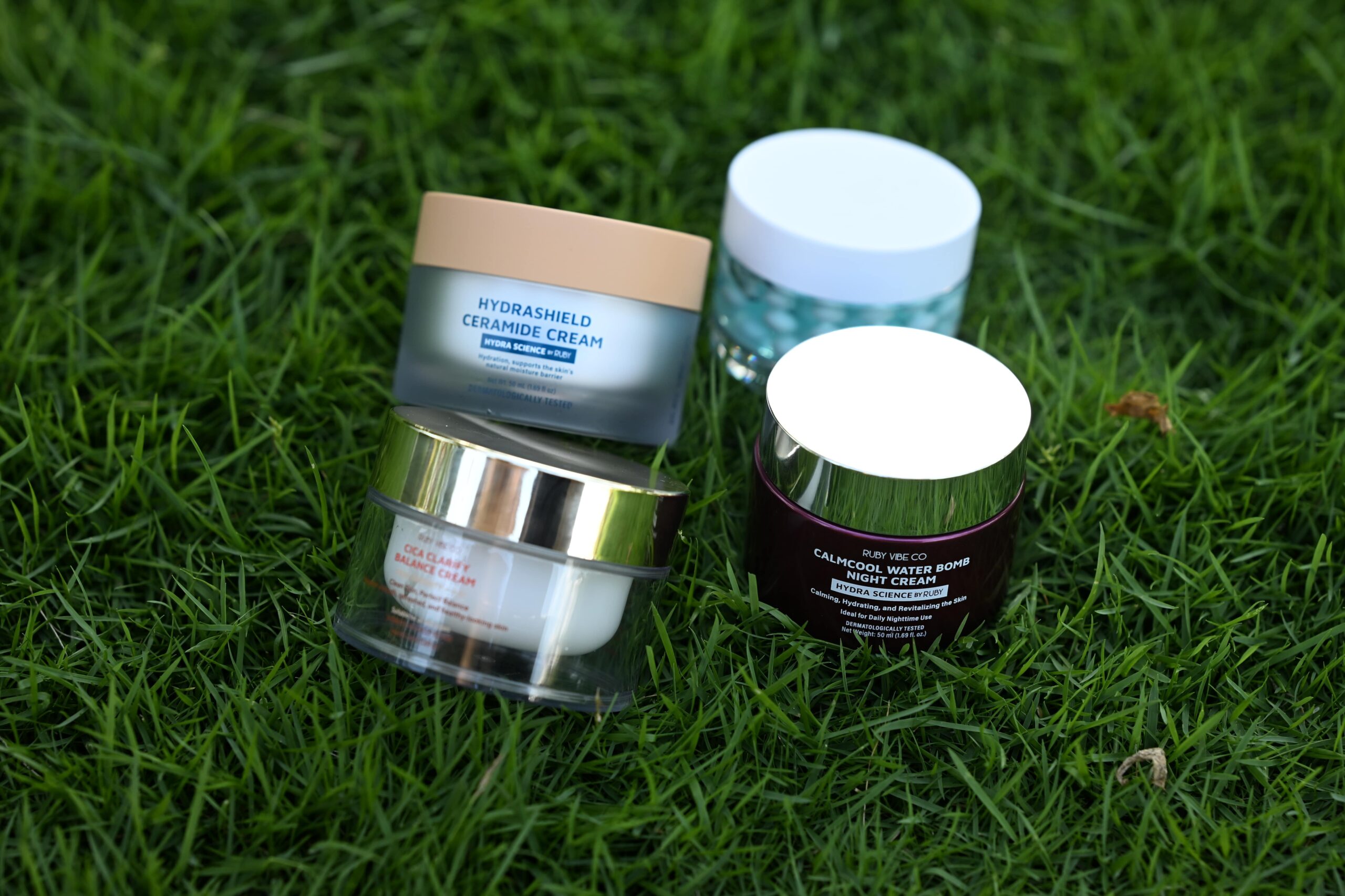 Four different moisturizers are displayed on a patch of grass, representing a selection of creams suitable for various oily skin types.