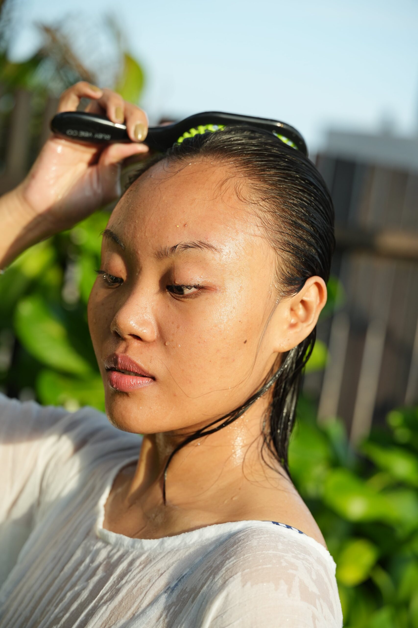 A person with wet, dark hair uses a black scalp brush to massage their scalp. This image visually demonstrates a step in a hair care routine for hair loss.