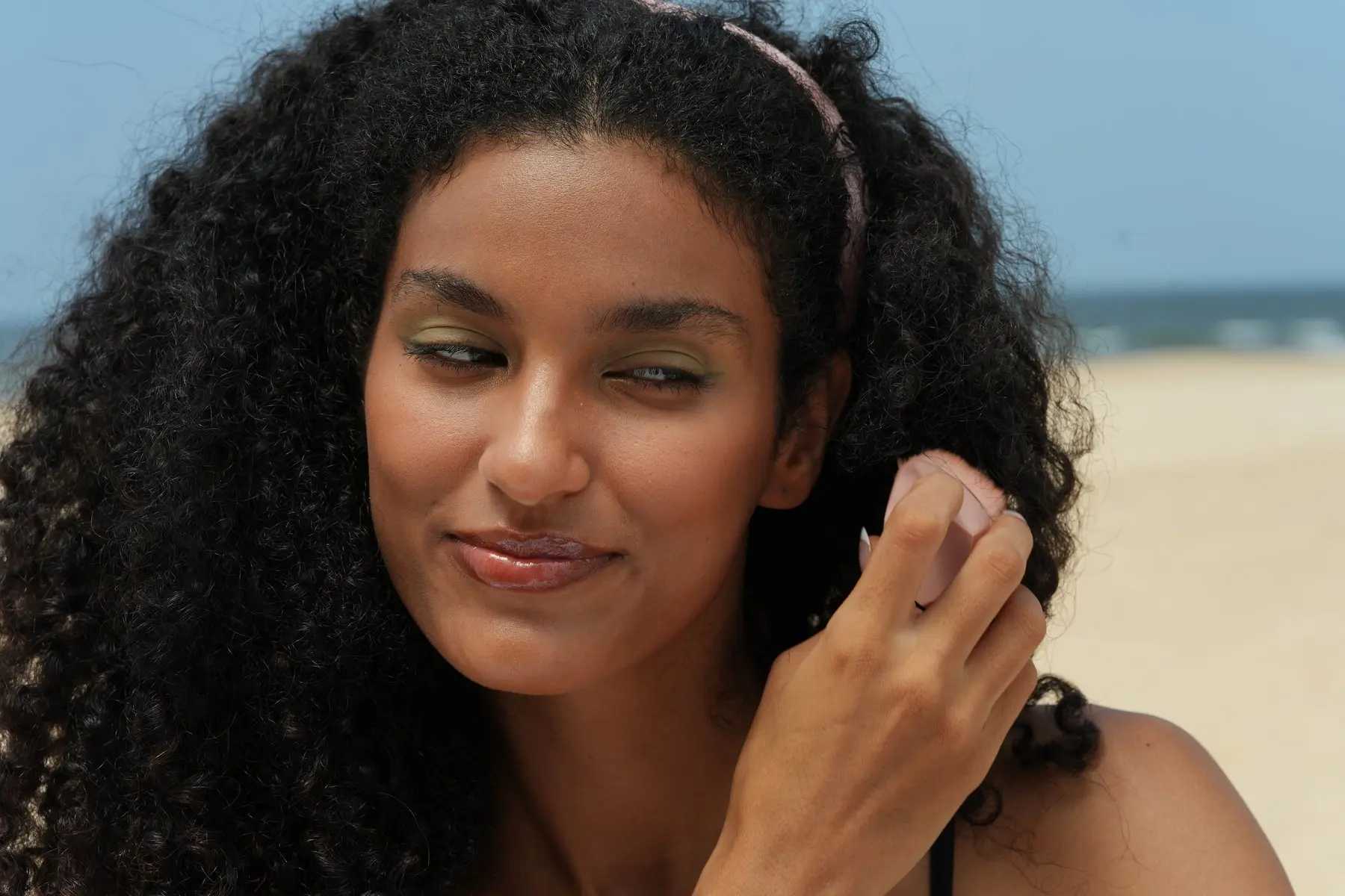 A woman with very curly black hair smiles warmly while standing outside. The image emphasizes healthy, voluminous hair, which is a desired outcome for those dealing with hair loss.