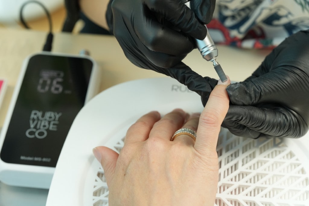 A hand with freshly painted nails curing inside a white Ruby Vibe Co UV/LED nail lamp, which is glowing with a blue light. 