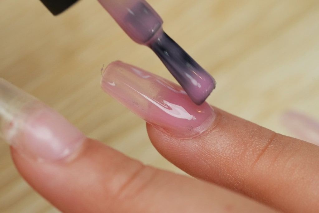 A nail technician wearing black gloves uses an electric file to prep a client's cuticle area for a gel manicure.