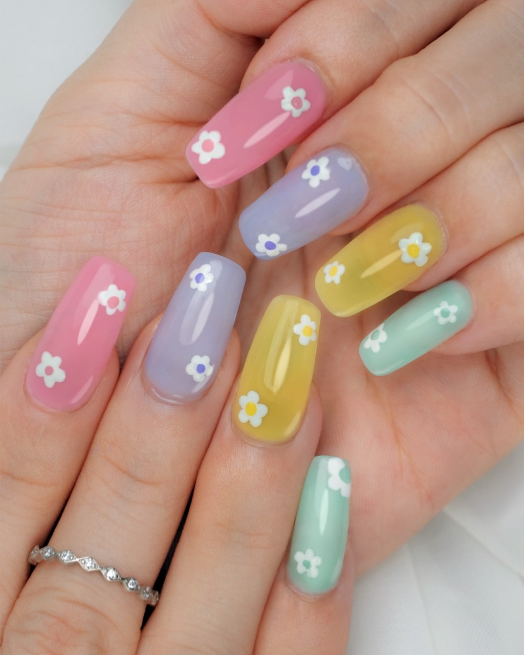 A close-up of a hand with a pastel rainbow manicure, each nail painted with small white daisy flowers.