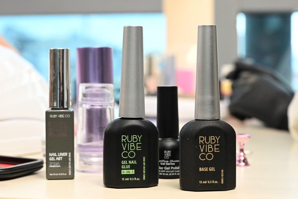 Several black bottles of Ruby Vibe Co nail gel products, including Base Gel and Gel Nail Glue, on a salon table.
